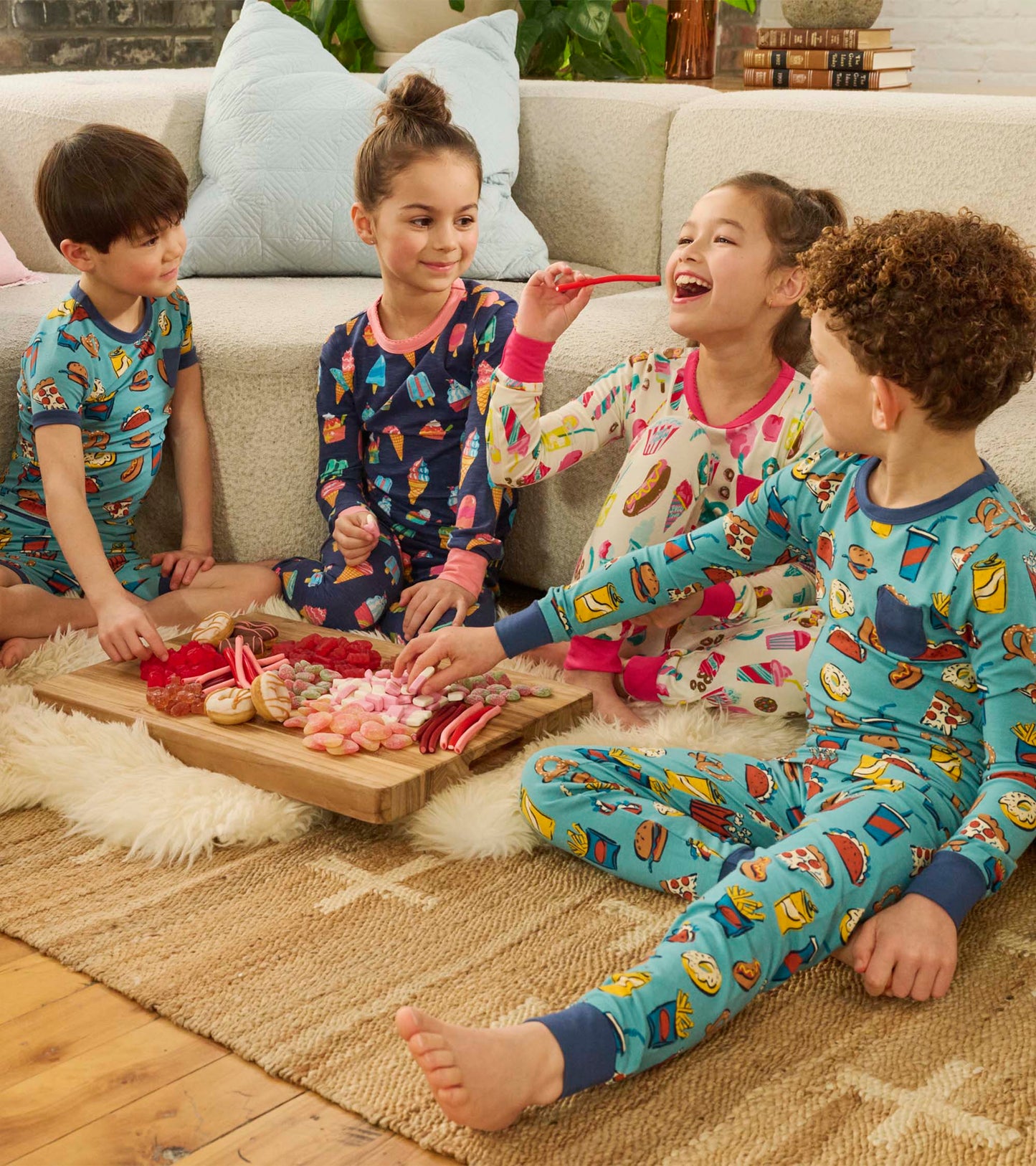 Colorful pyjama set featuring ice cream and treat patterns, worn by kids sitting on a rug with a snack platter.