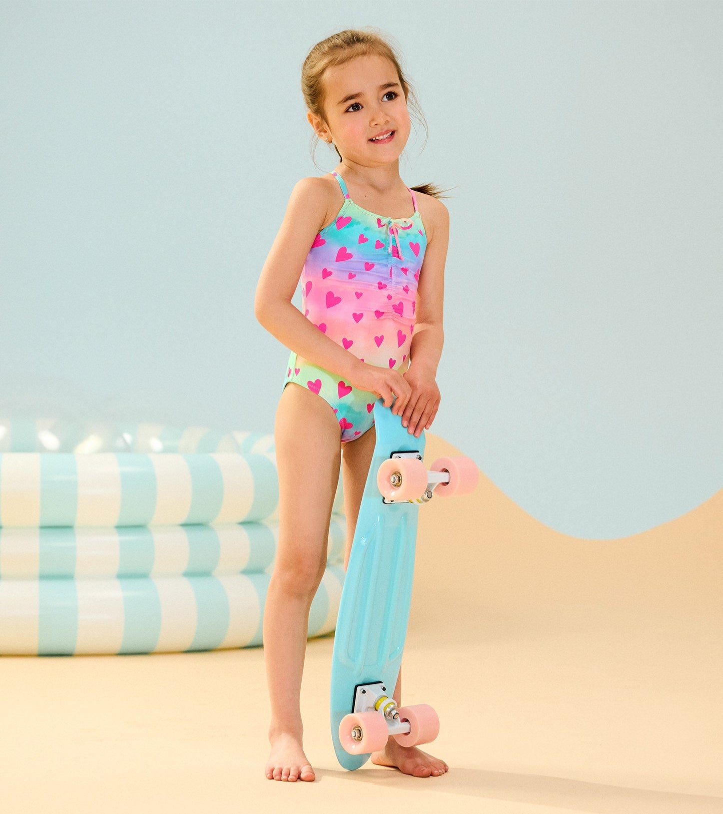Colorful swimsuit featuring a ruched front with a kaleidoscope heart pattern, paired with a blue skateboard.