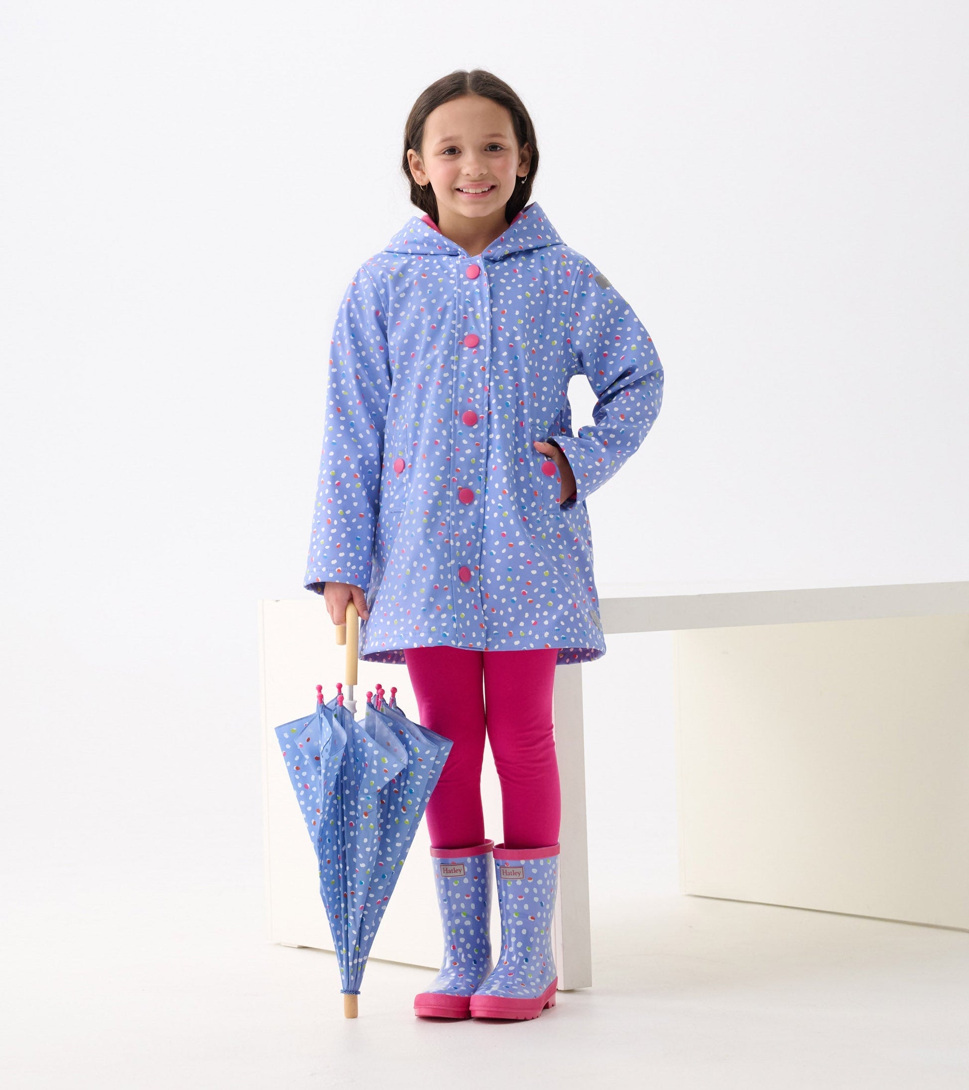 Shiny blue wellies with colorful dots, paired with a matching raincoat and pink leggings, held with an umbrella.