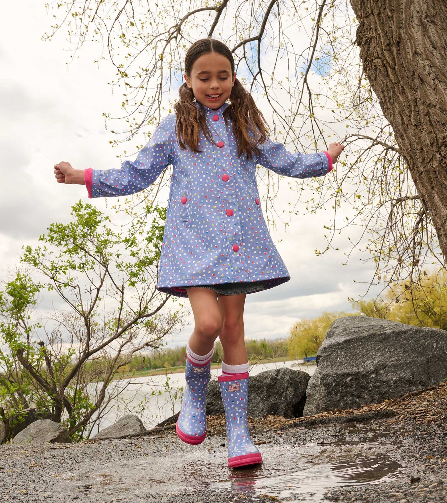 Light blue button-up raincoat with colorful polka dots, paired with matching rain boots, worn by a girl outdoors.