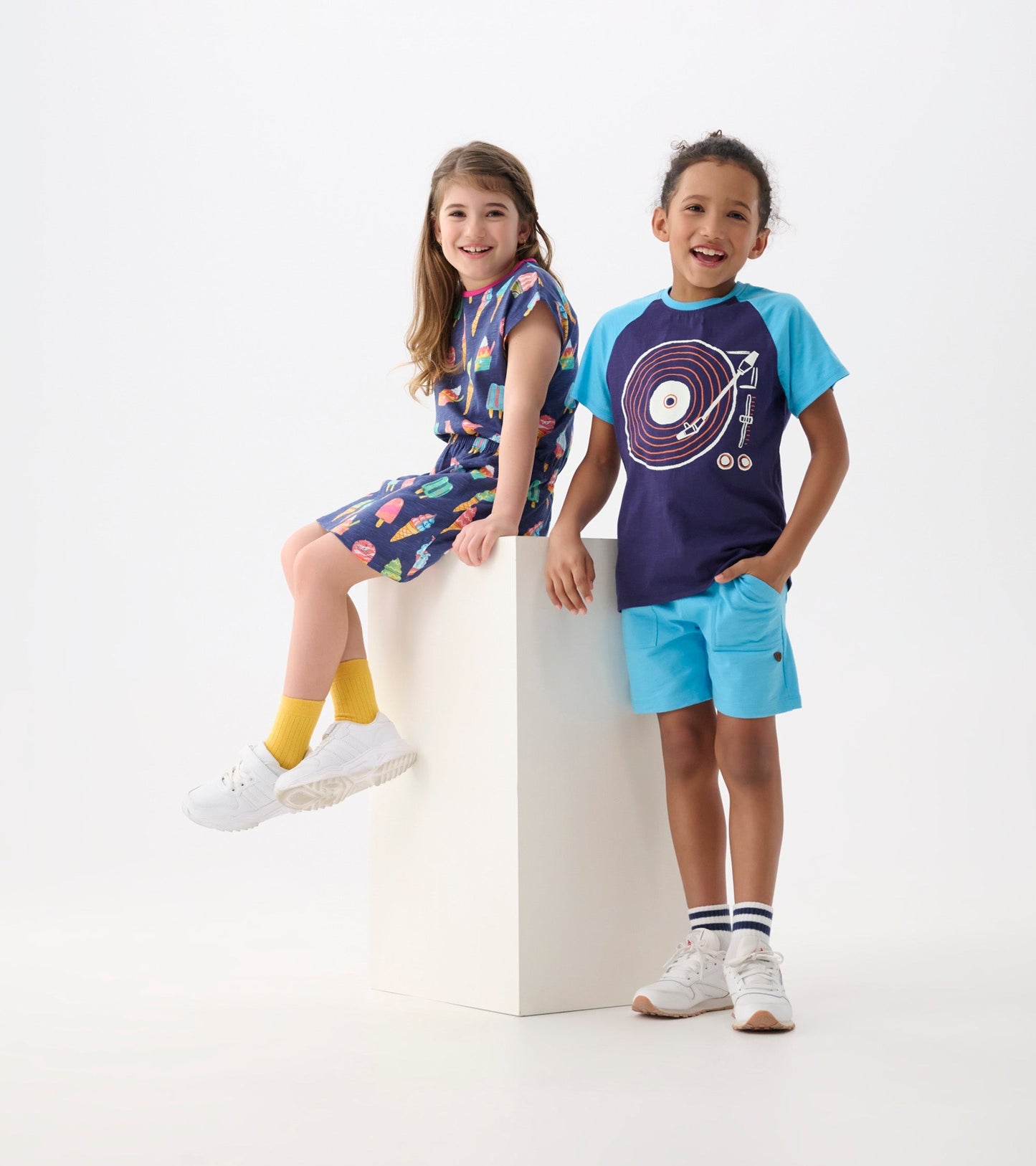 Aqua blue relaxed shorts with pockets, worn by a boy standing next to a girl in a colorful dress.