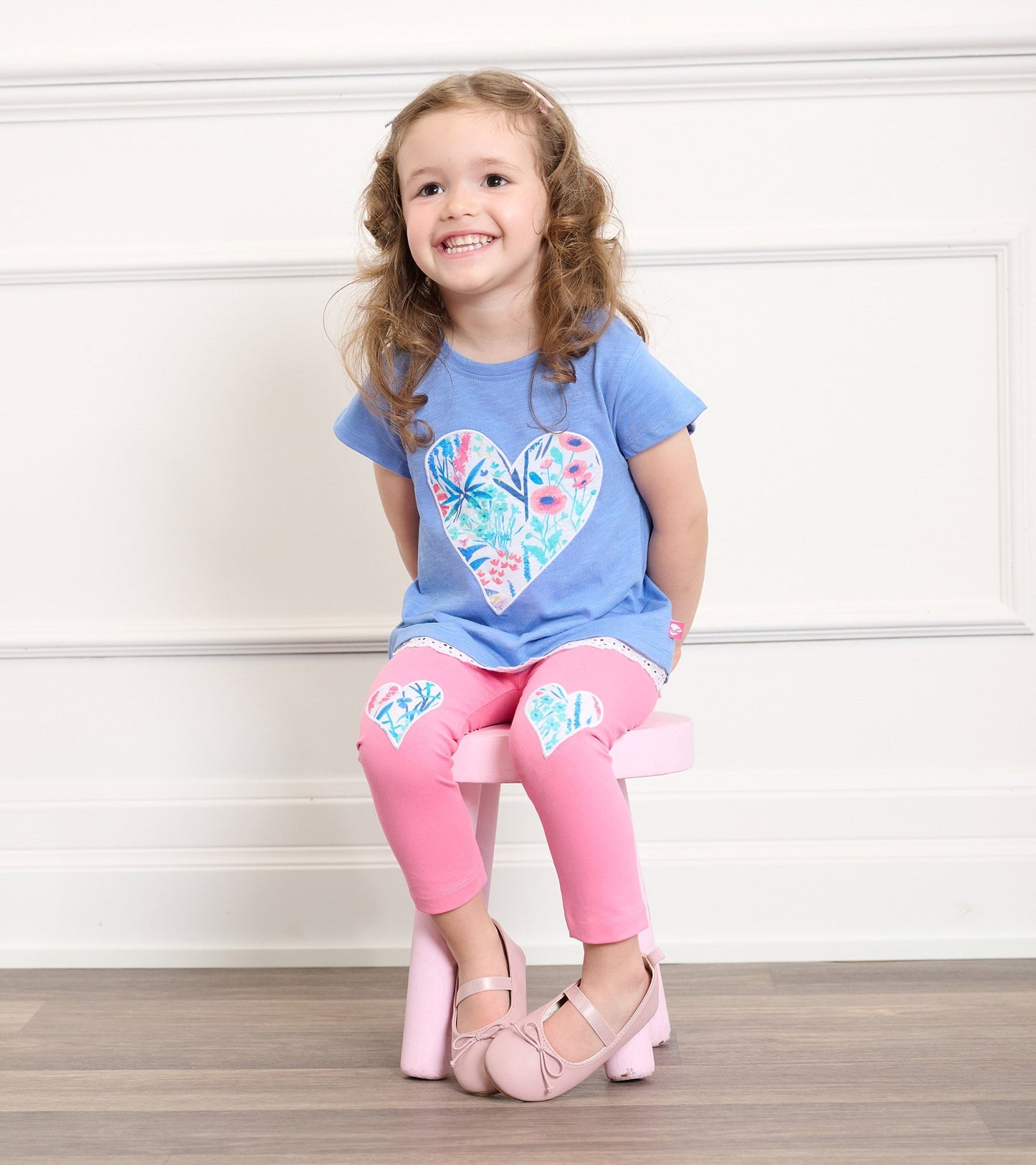 Blue t-shirt with floral heart design, paired with pink leggings featuring heart patches, worn by a smiling girl.