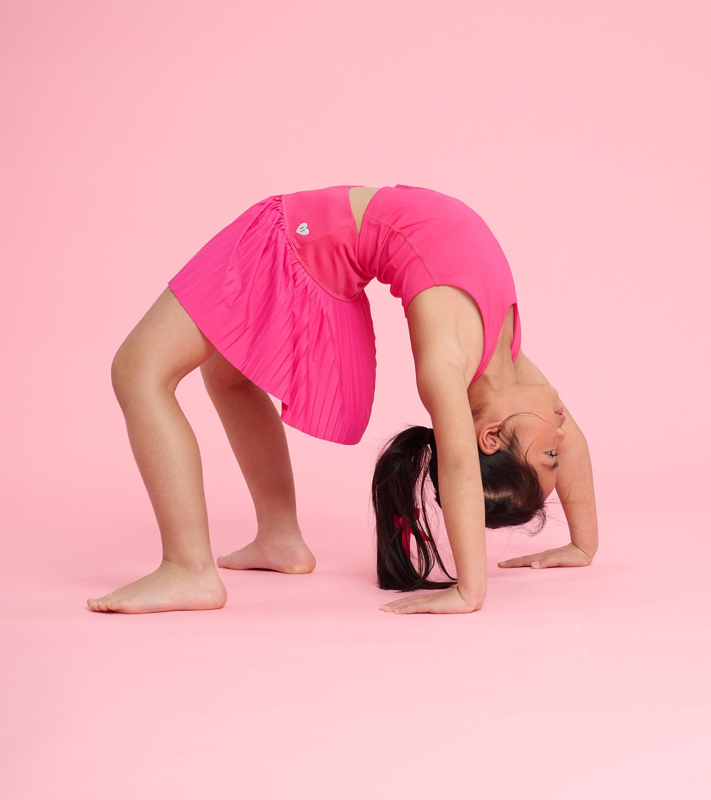 Bright pink sporty skort with pleated design, worn by a girl in a playful pose against a pink background.