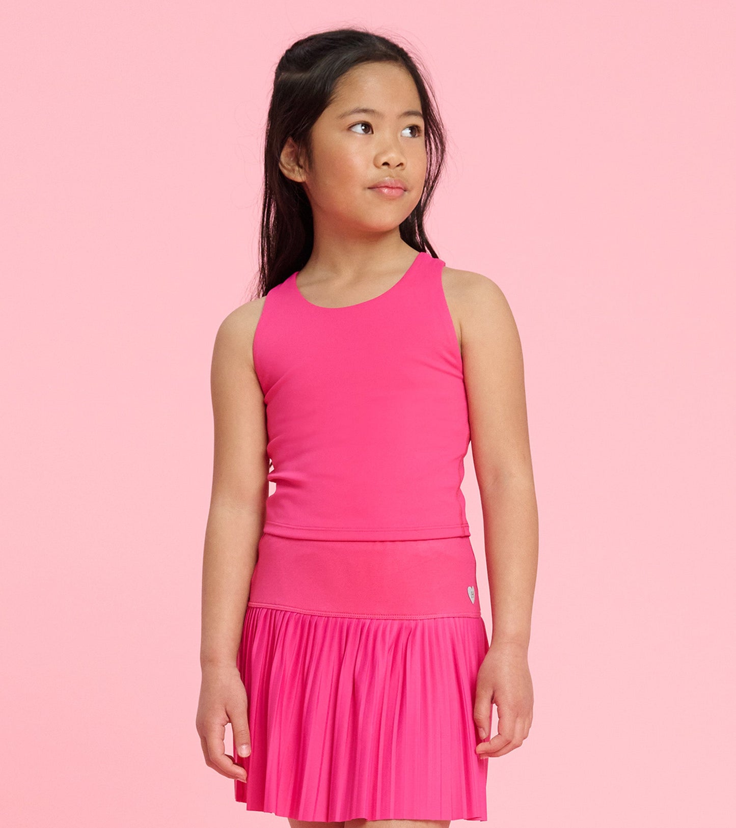 Bright pink tank top with a fitted design, worn by a girl, paired with a matching pleated skirt.