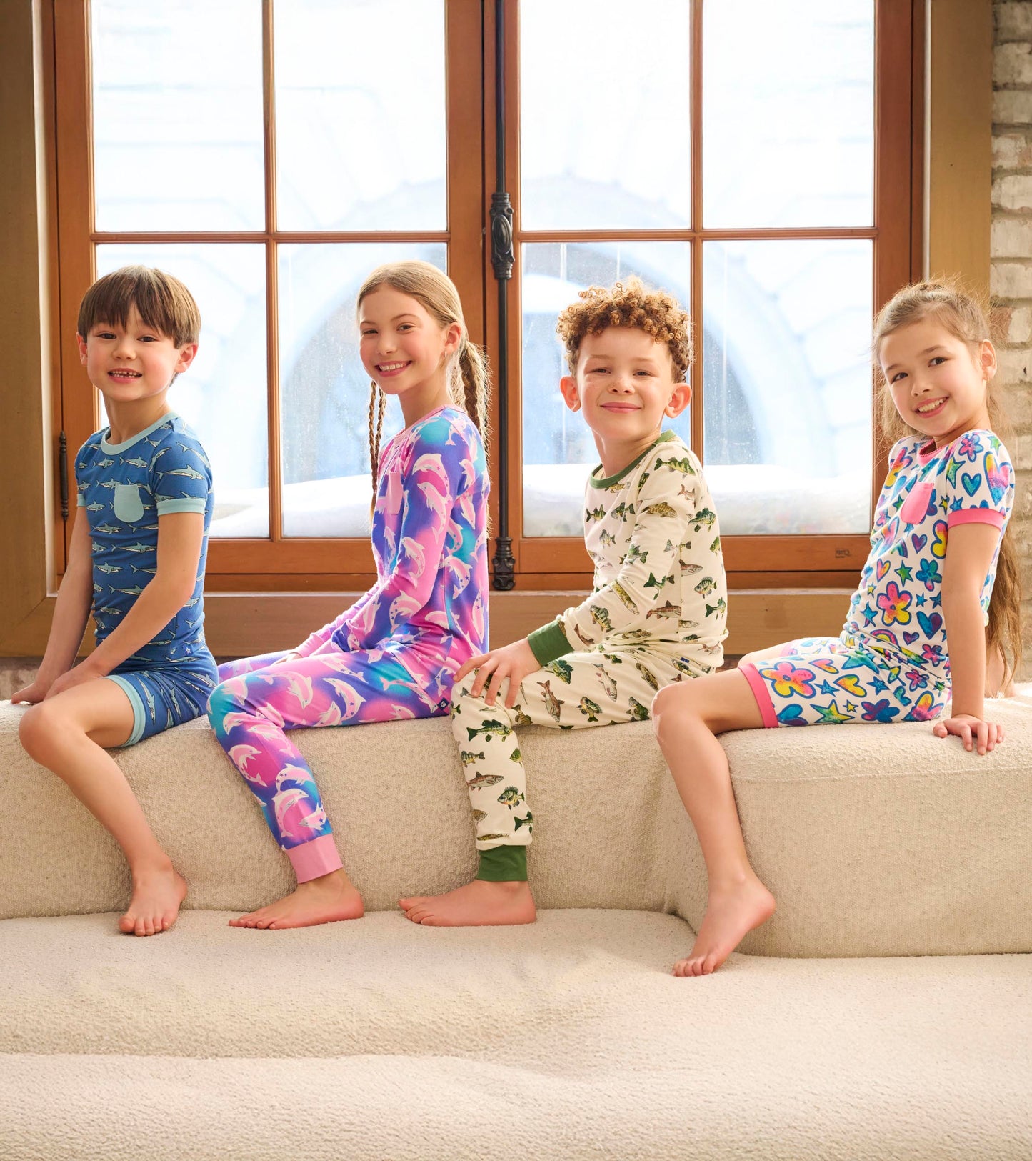 Four children sitting on a couch, wearing colorful bamboo short pyjama sets with various playful patterns.
