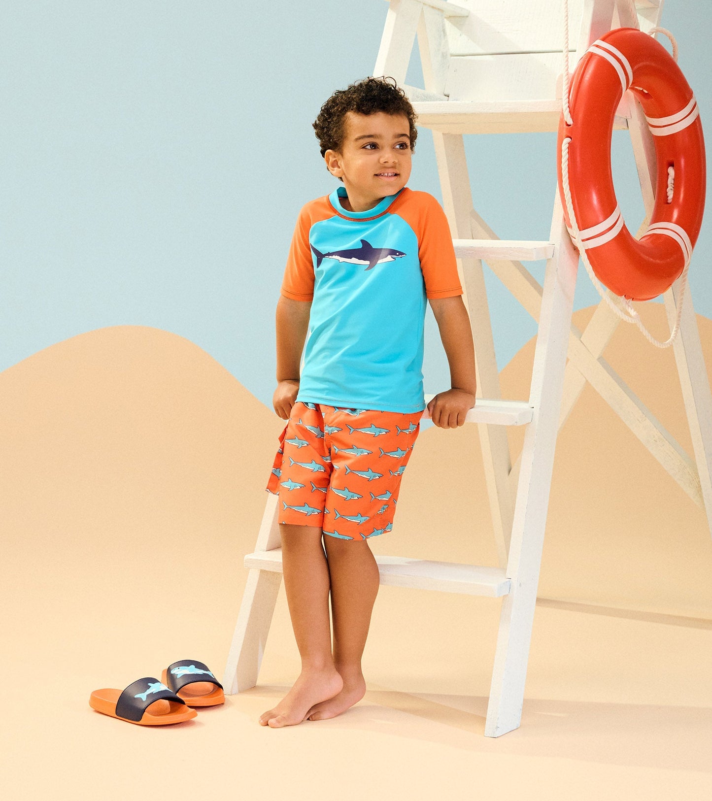Boys' board shorts in orange with blue shark pattern, paired with a turquoise rash guard, perfect for beach activities.