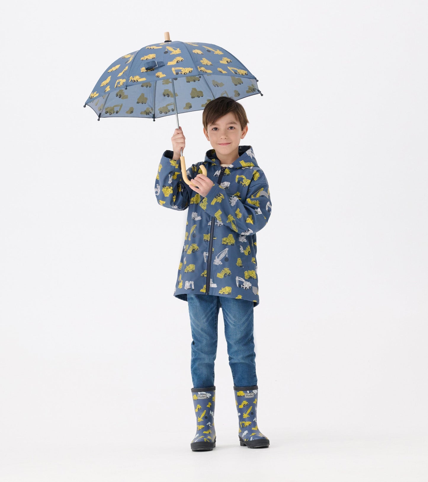 Matte wellies in gray with yellow construction vehicle patterns, worn by a boy holding a matching umbrella.