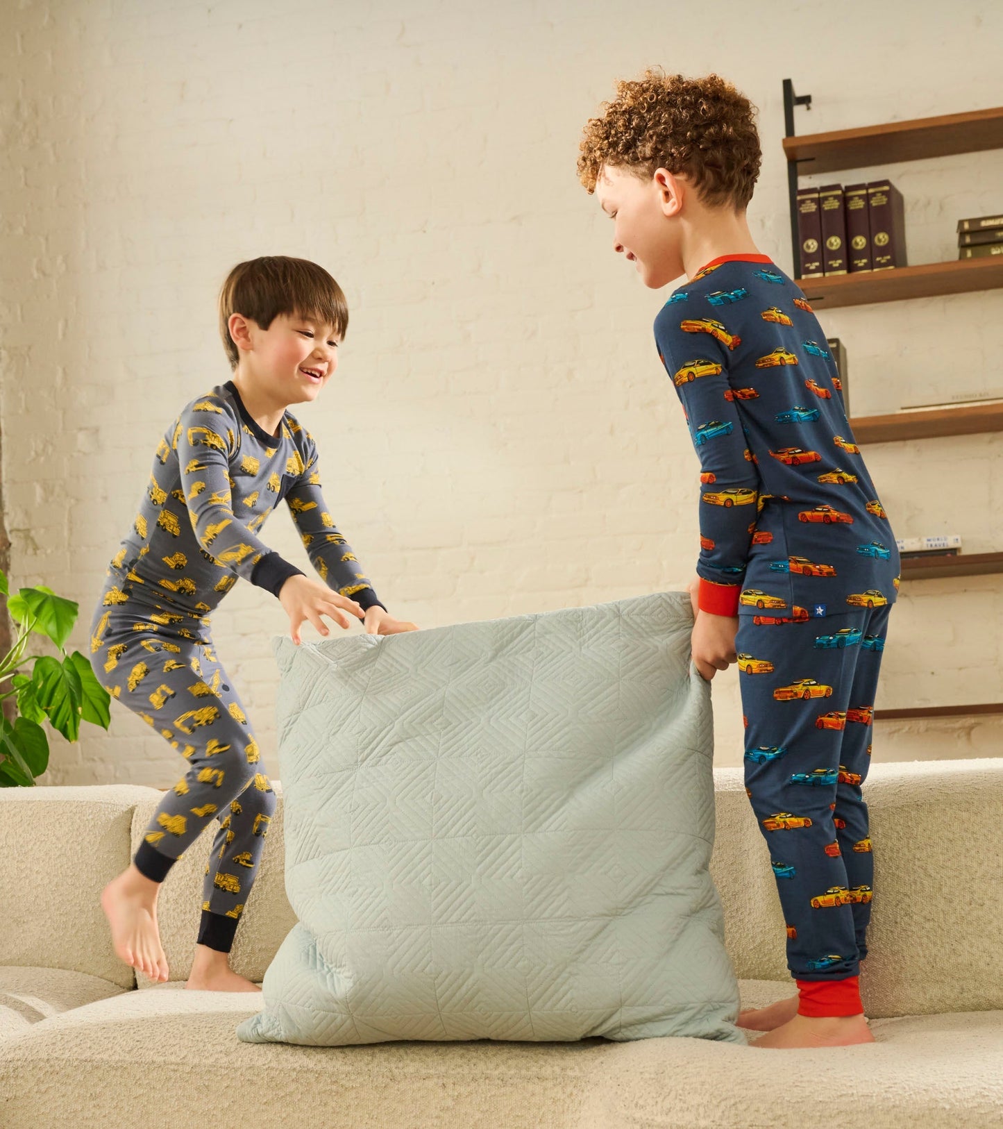 Boys' bamboo pyjama set featuring colorful car patterns, worn by two children playing with a large pillow on a couch.