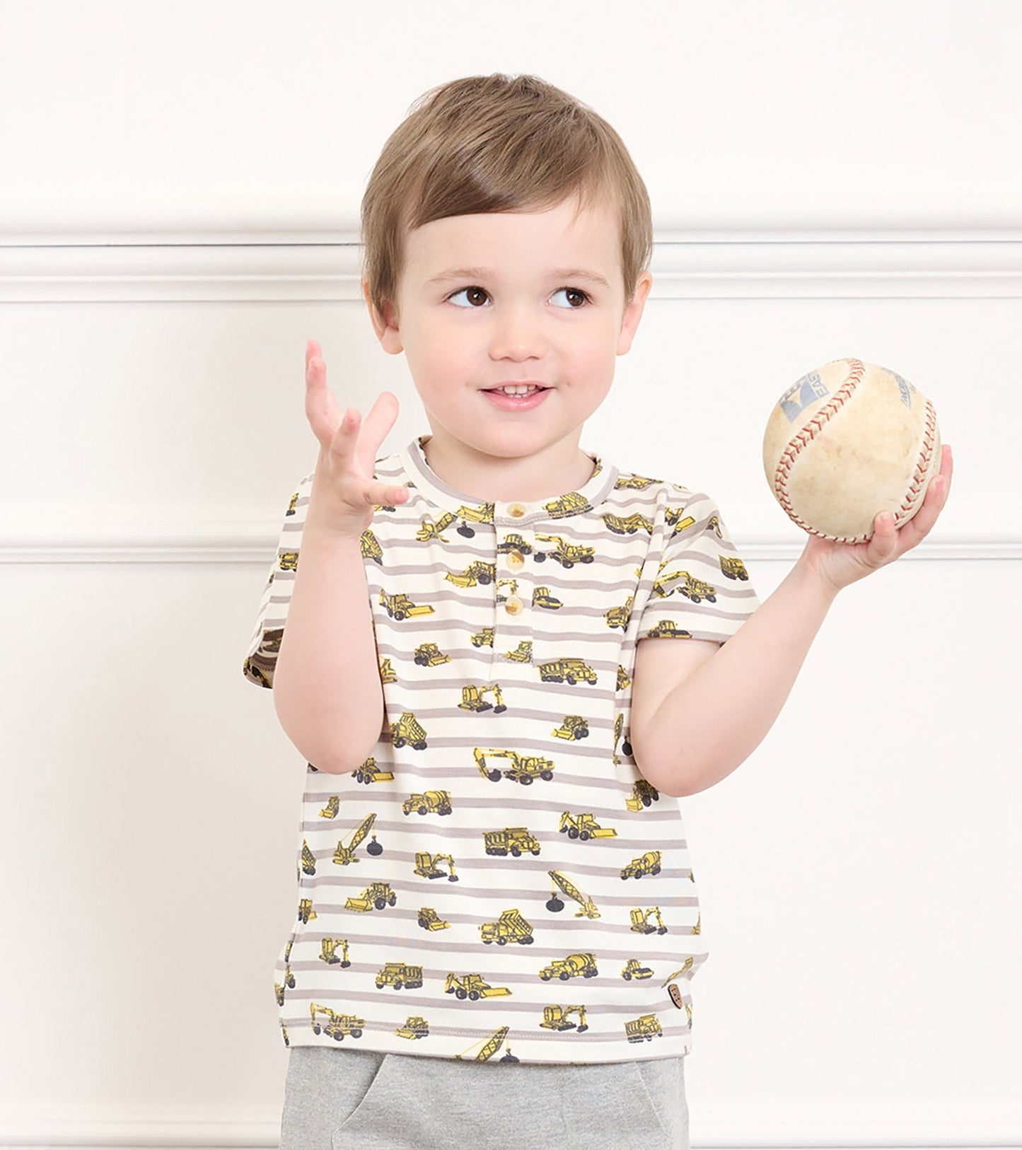 Bamboo henley shirt for toddlers featuring yellow construction vehicles on a striped background, short sleeves, and a button…