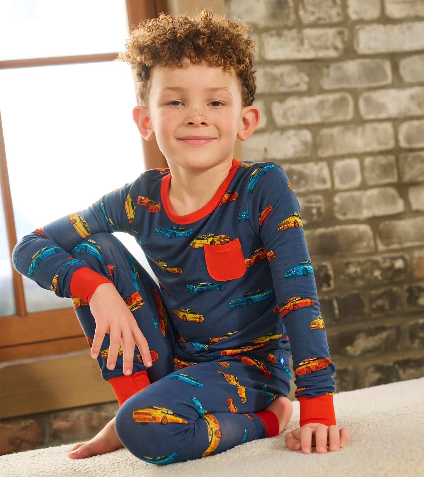 Boys' bamboo pyjama set featuring a blue background with colorful car prints and red accents on the cuffs and pocket.