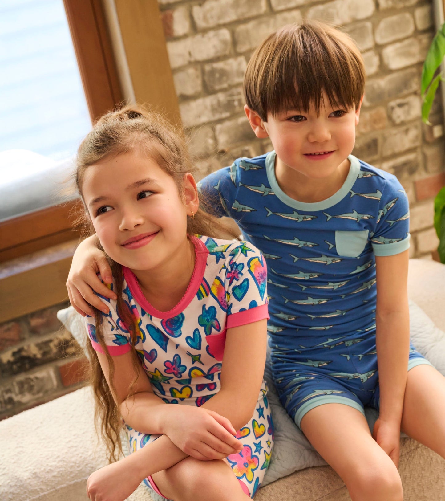 Colorful short pyjama set featuring watercolour doodles on a white background, worn by a girl and a boy.