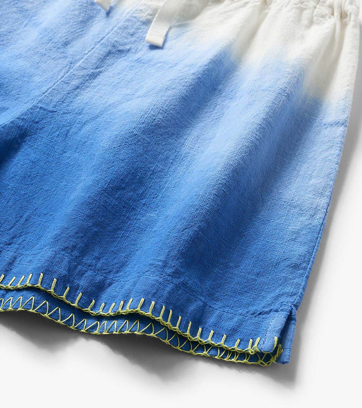 Blue and white dip-dye woven shorts with lime green stitched hem, close-up view