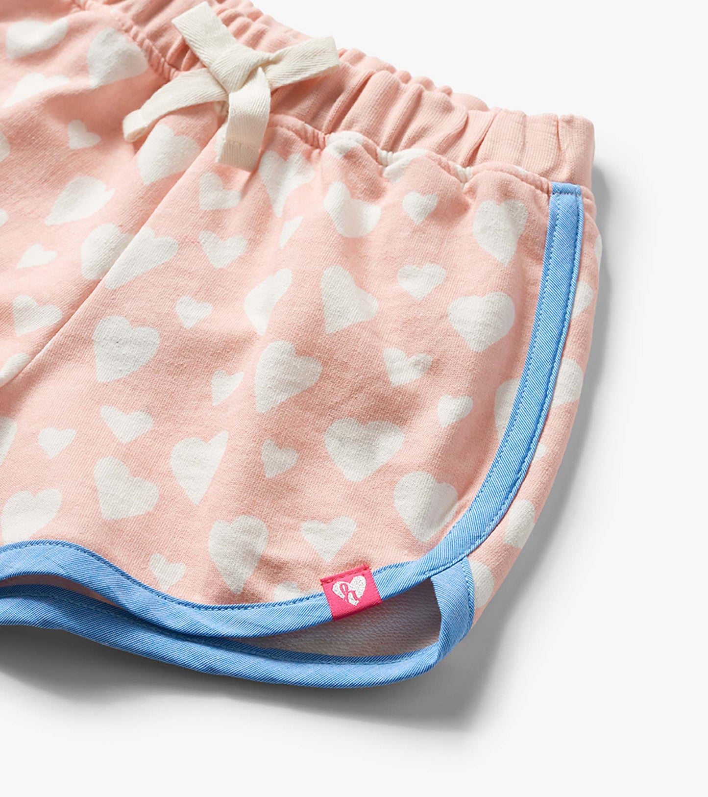 Pink shorts with white heart print, blue trim, and drawstring waistband, close-up view