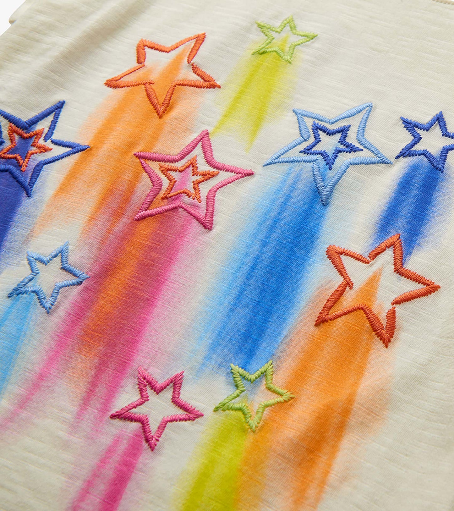 Close-up of cream tee fabric with colorful embroidered stars and rainbow streaks