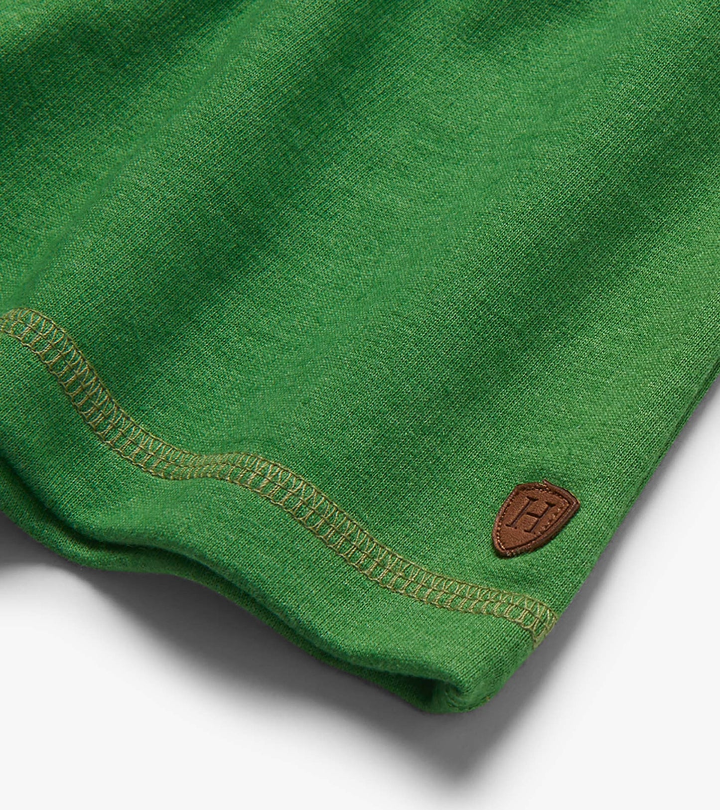 Close-up of green knit shorts hem with contrast stitching and small brown patch logo