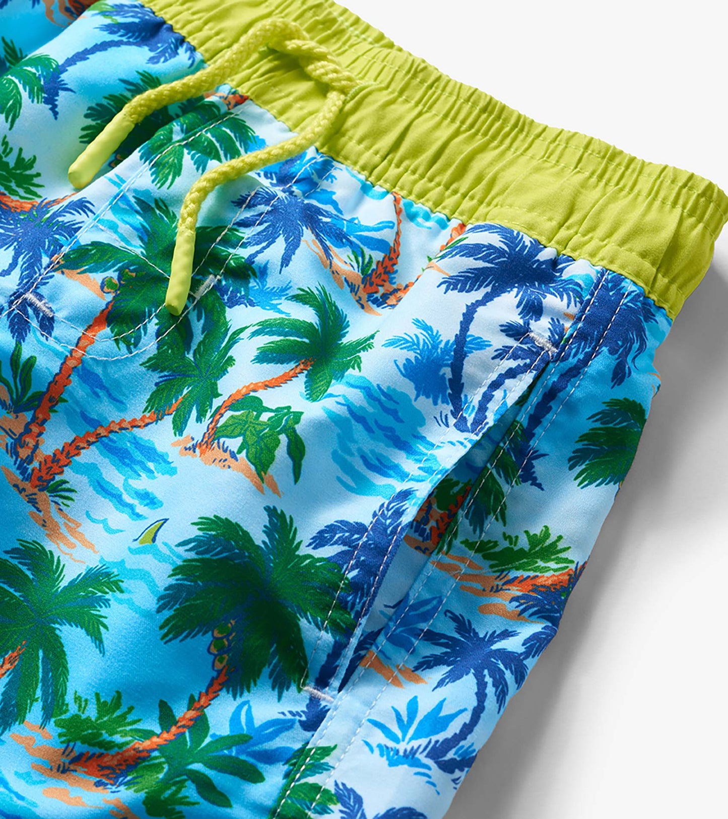 Close-up of boys' swim trunks with blue tropical palm print, lime green waistband, and drawstring.