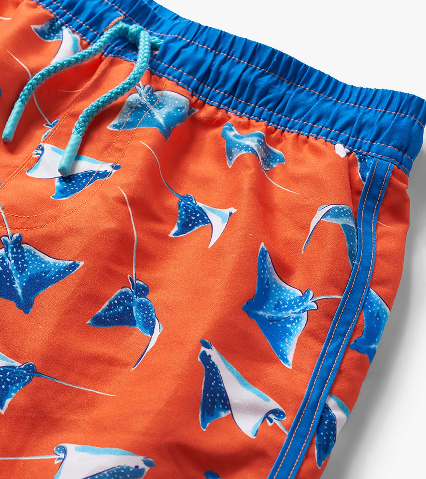 Orange boys swim trunks with blue stingray print, drawstring waist, and blue trim close-up