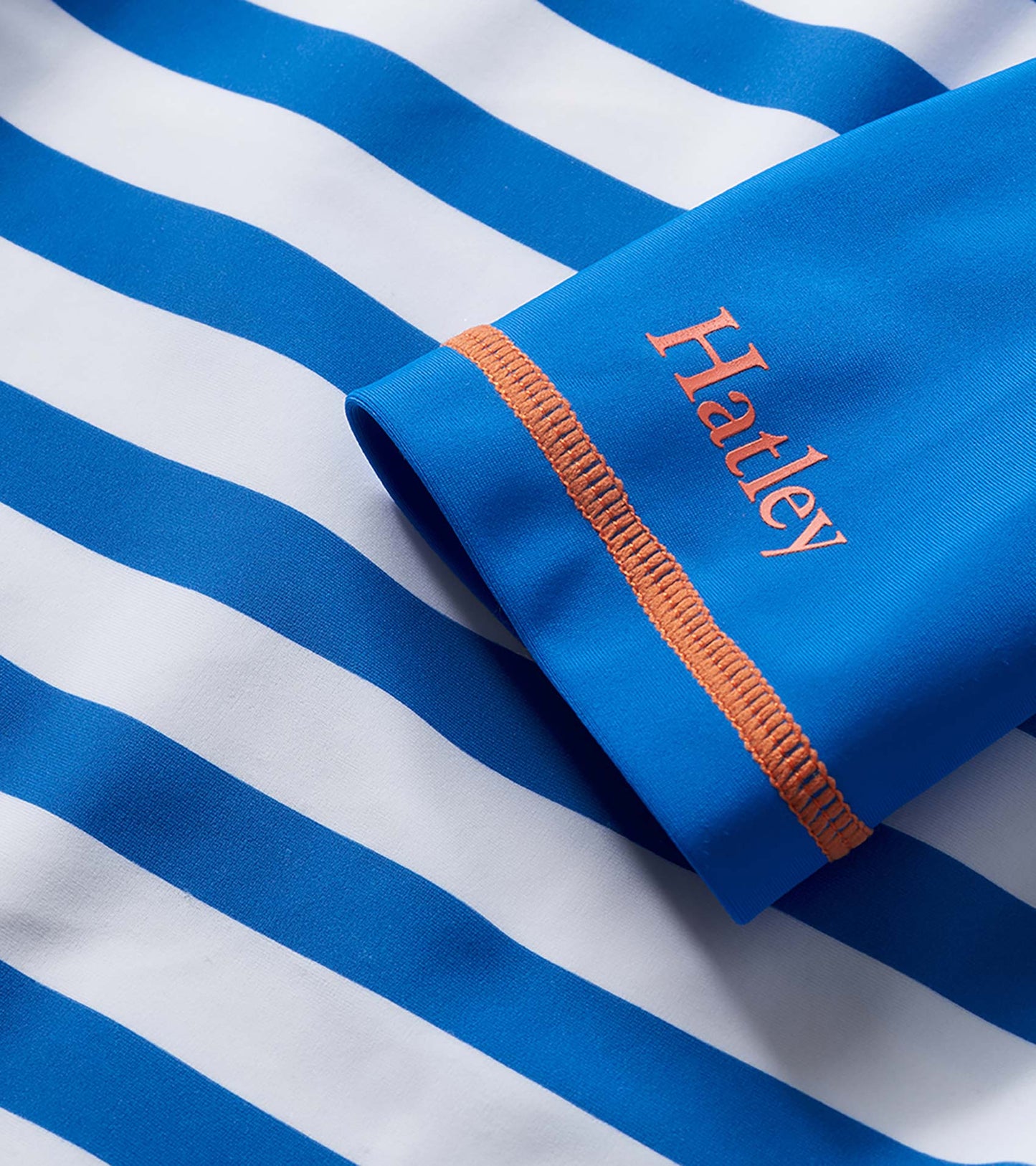 Blue and white striped short sleeve rashguard with orange stitching and logo detail, close-up view