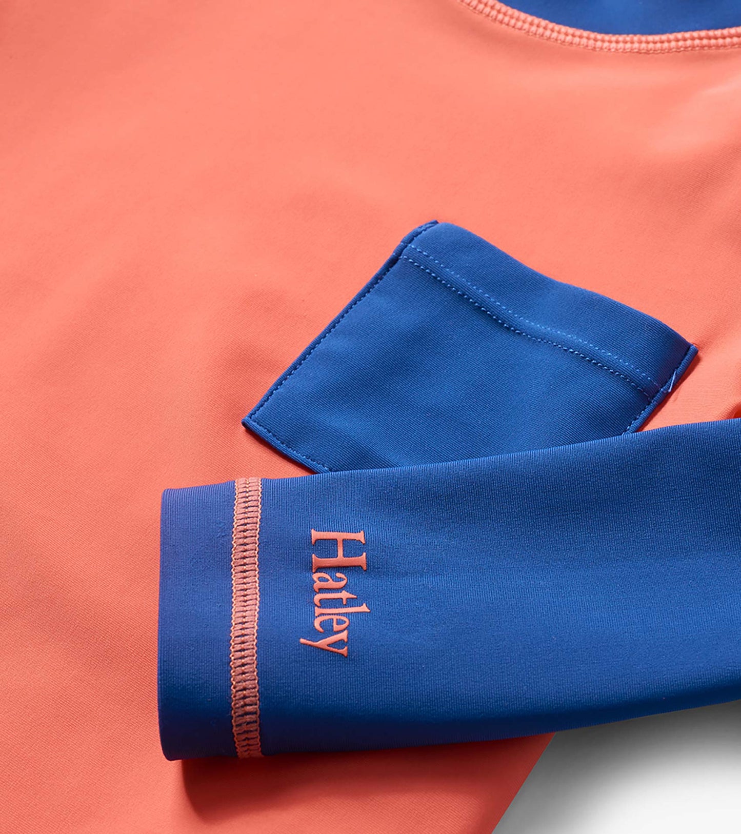 Coral and navy long sleeve boys rashguard with blue sleeve and logo detail, close-up view