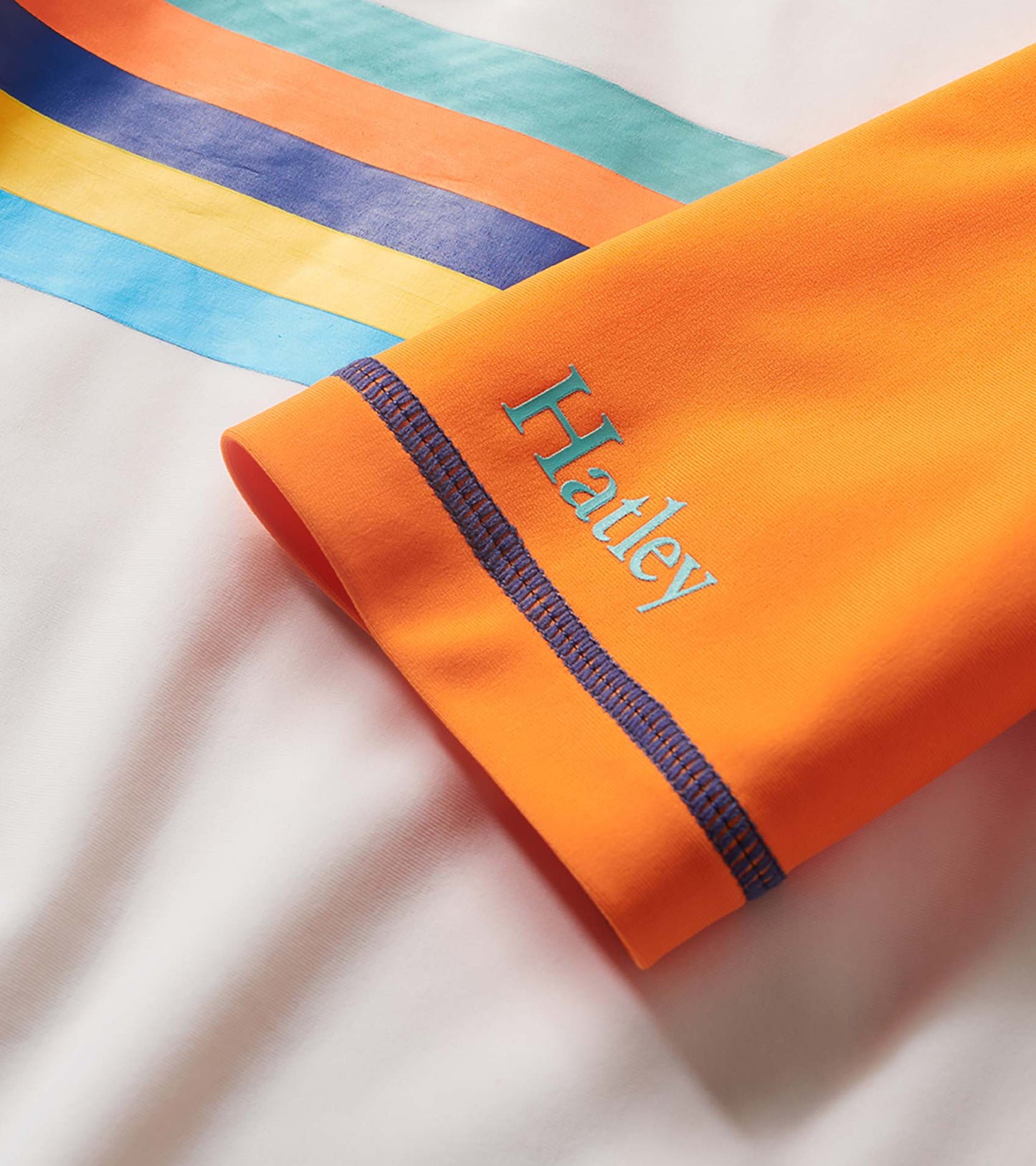 Orange boys' rashguard with long striped sleeves and blue seam stitching, folded on white background
