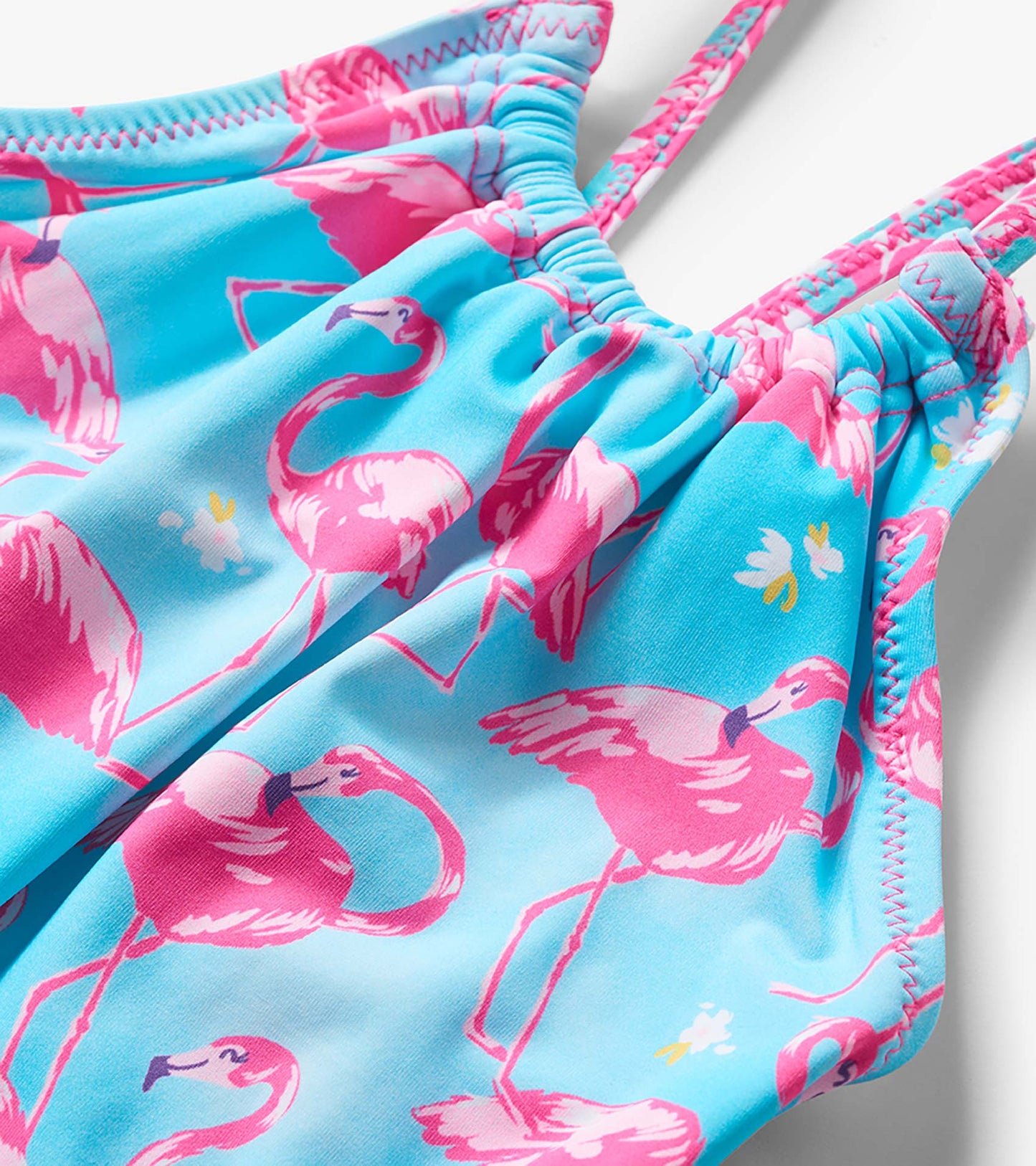 Close-up of a blue girls' one-piece swimsuit with pink flamingo print and pink zigzag trim, front view
