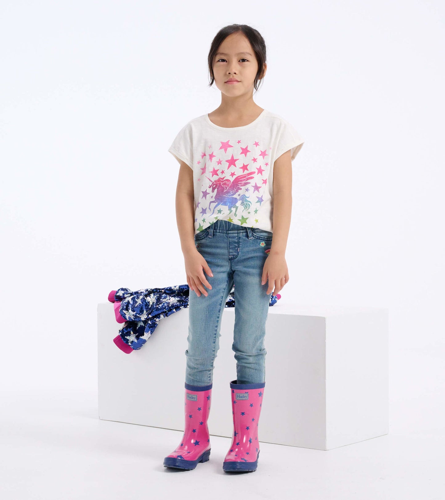 Relaxed white t-shirt featuring colorful star and unicorn graphic, paired with blue jeans and pink rain boots.