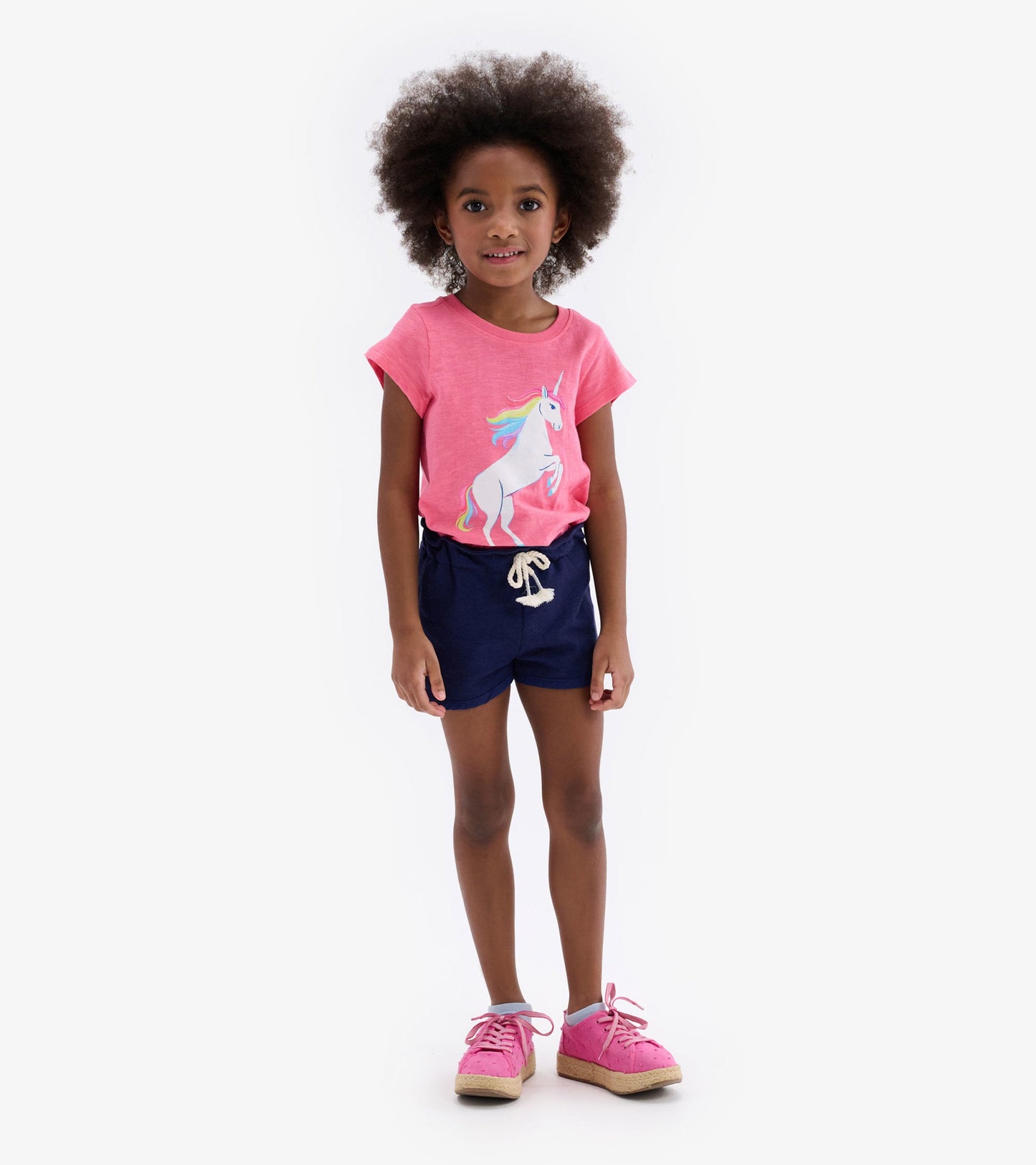 Pink short-sleeve tee featuring a unicorn graphic, paired with navy shorts and pink sneakers.
