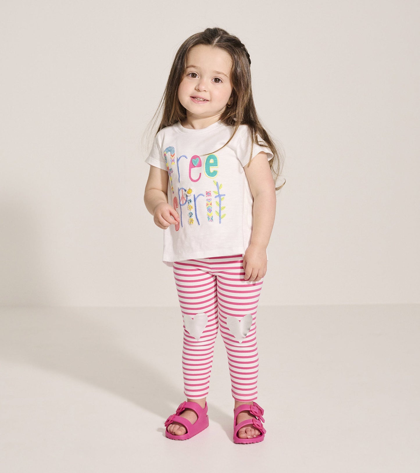 White graphic tee with colorful "Free Spirit" text, paired with pink and white striped leggings and pink sandals.