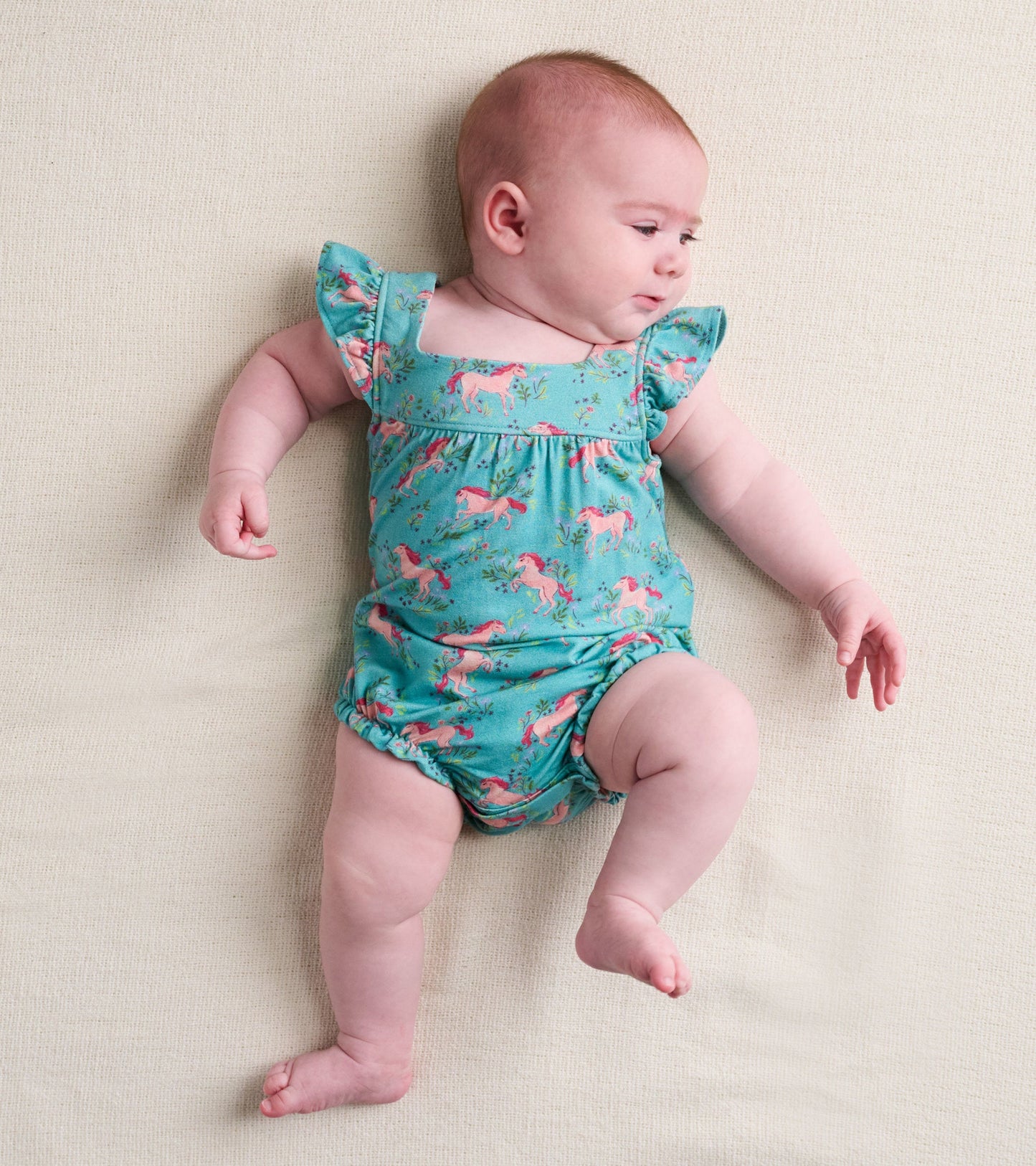 Turquoise baby bubble one-piece with ruffled sleeves and a playful unicorn print, suitable for infants.