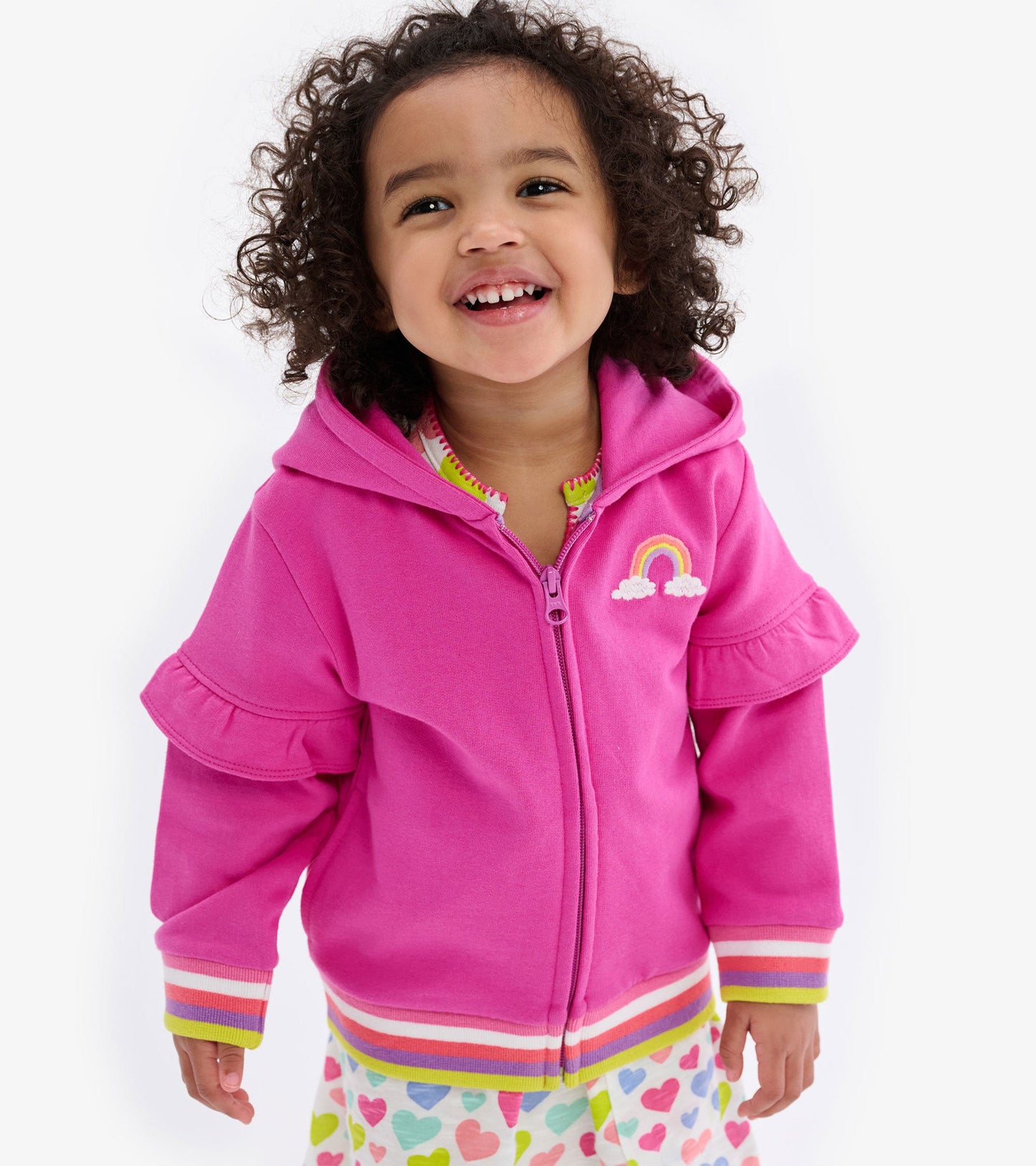 Pink hoodie with flutter sleeves, rainbow embroidery, and striped cuffs, worn by a smiling toddler.