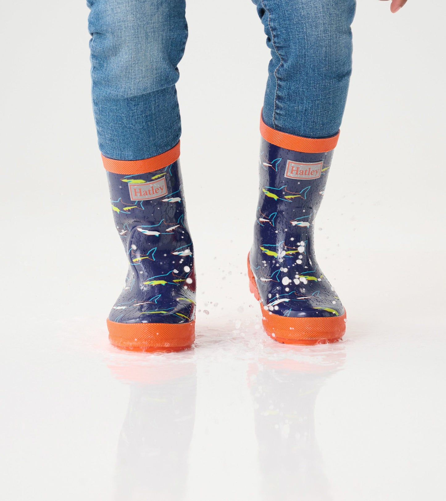 Shiny navy wellies with colorful shark patterns and orange trim, splashing in water, suitable for kids.
