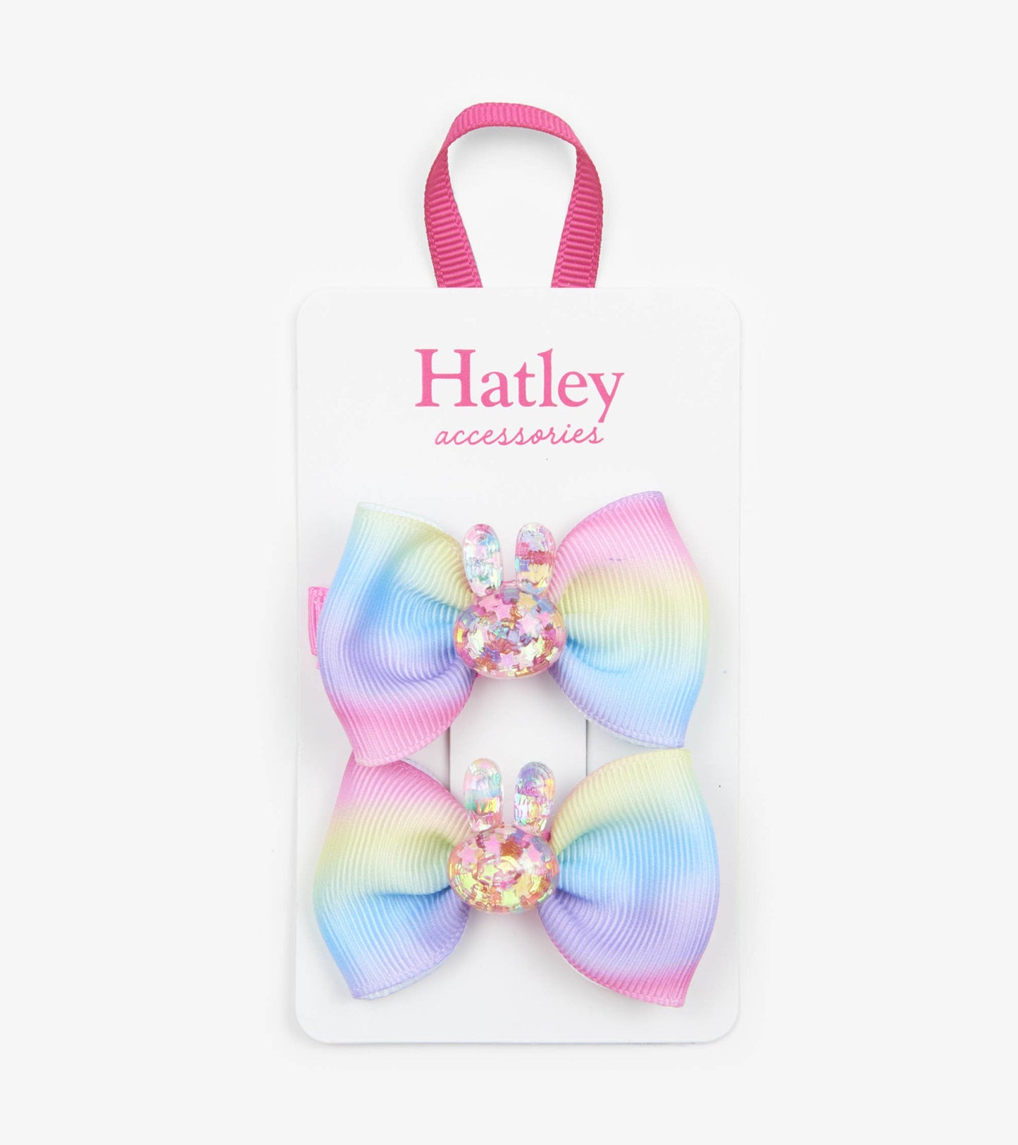 Two pastel rainbow hair clips shaped like bows with glittery bunny accents, attached to a display card.