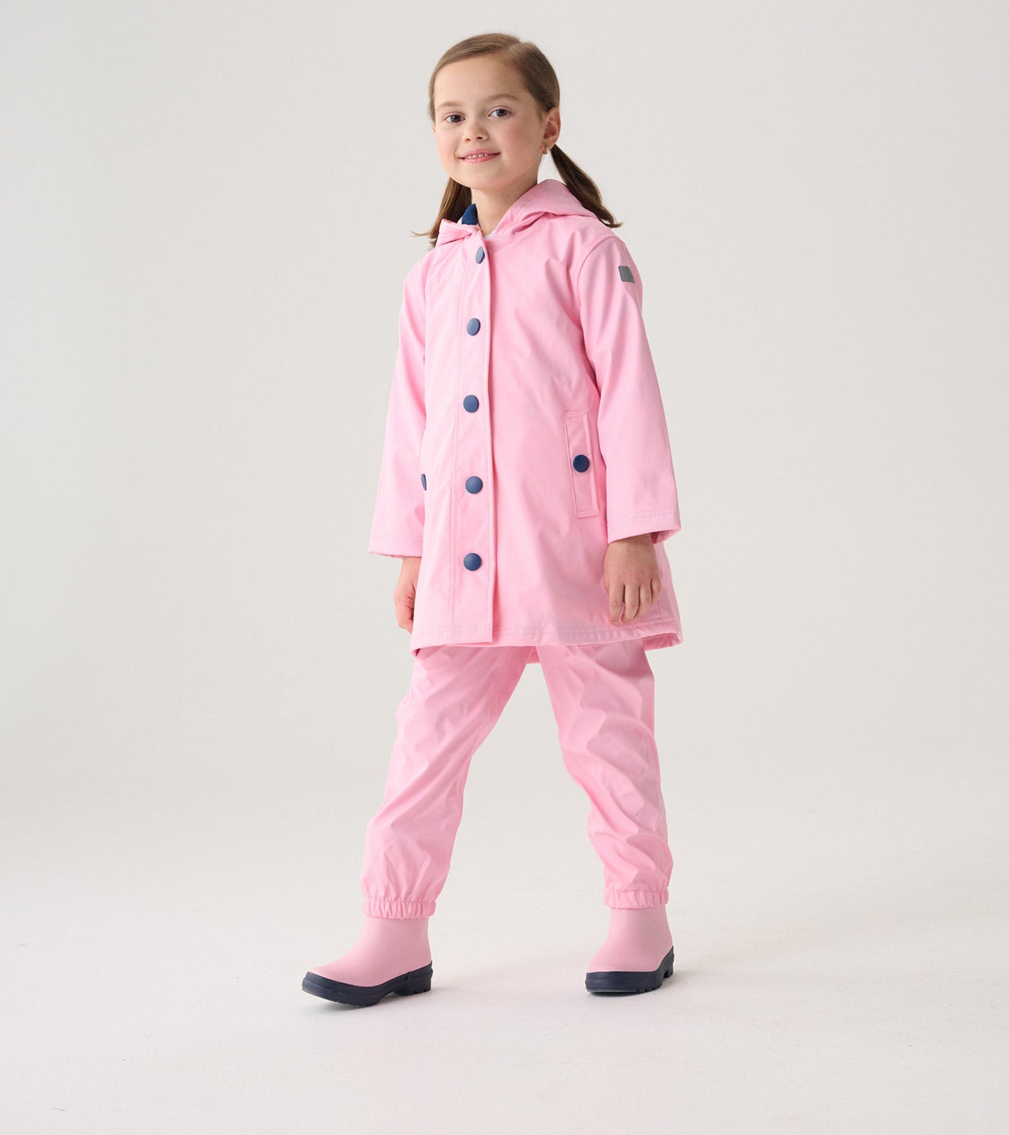 Pink waterproof rain pants with elastic cuffs, paired with a matching jacket and rubber boots, suitable for kids.