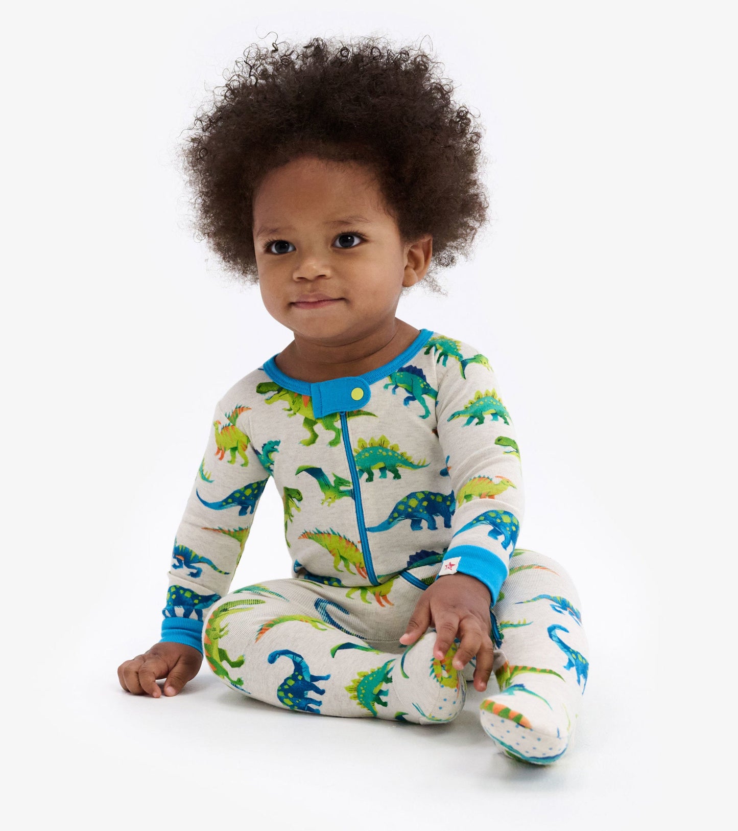 Colourful dinosaur print footed sleeper with blue accents, designed for infants, featuring long sleeves and a snap closure.