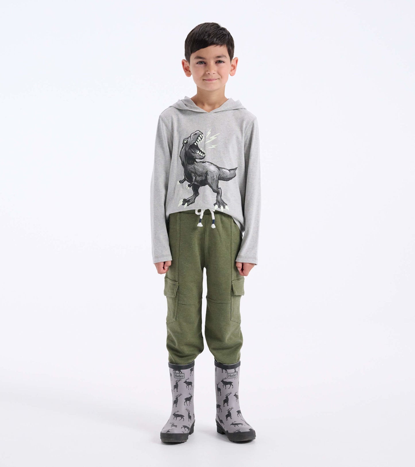 Gray long sleeve hoodie tee featuring a dinosaur graphic, paired with green cargo pants and patterned rain boots.