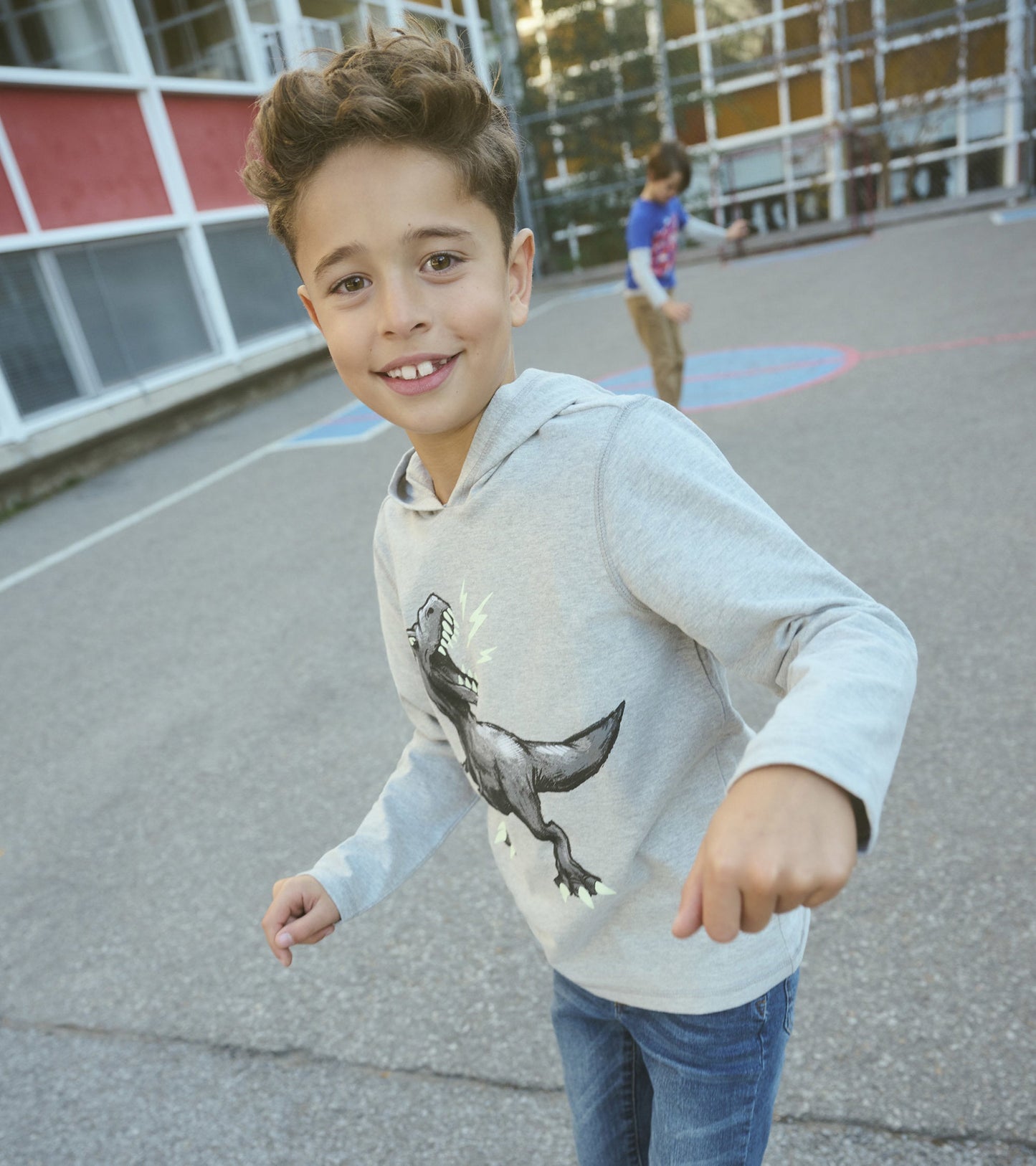 Gray long sleeve hoodie featuring a dinosaur graphic, worn by a boy playing outdoors.