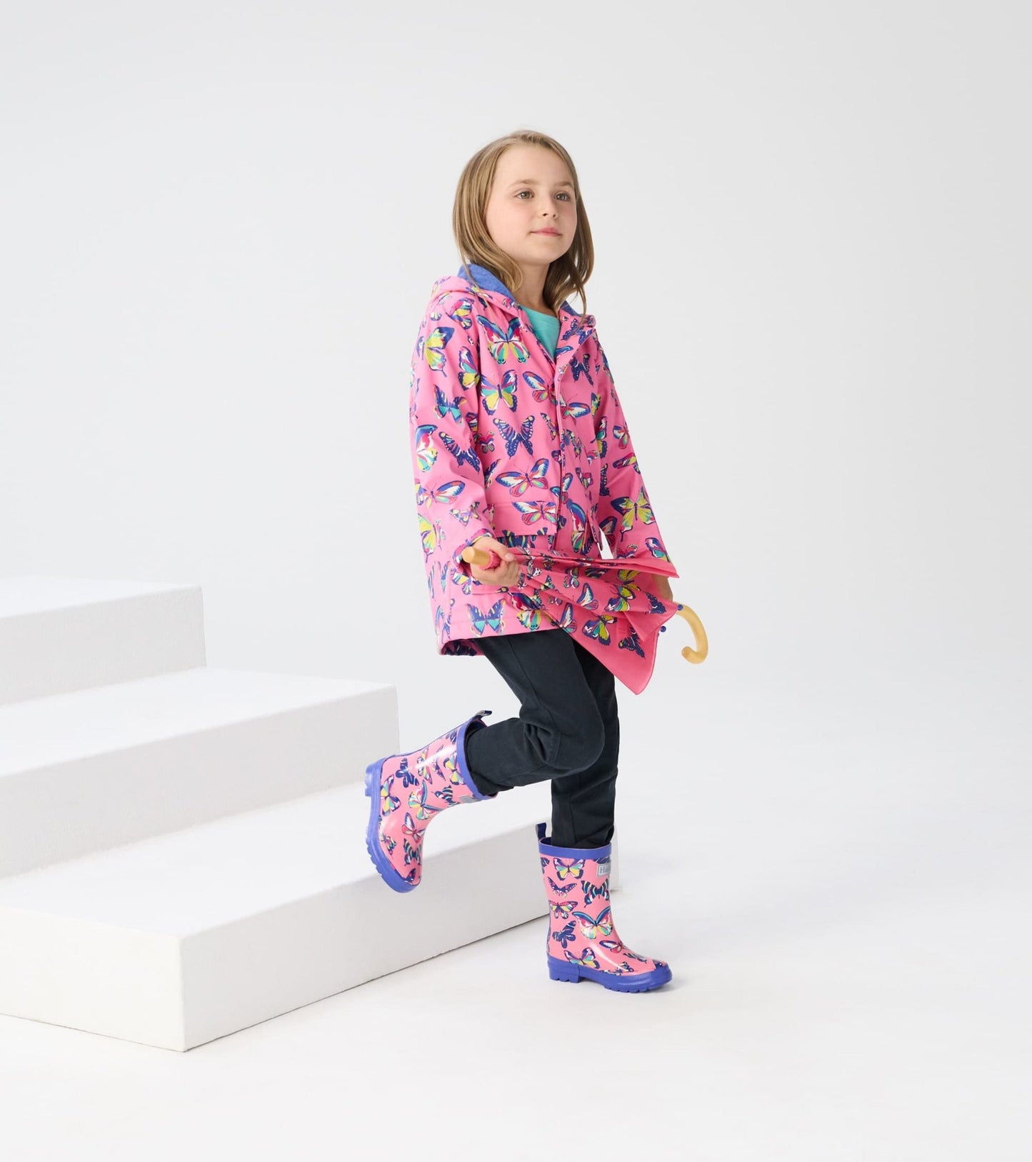 Pink wellies with vibrant butterfly patterns and purple soles, worn by a child in a colorful raincoat.