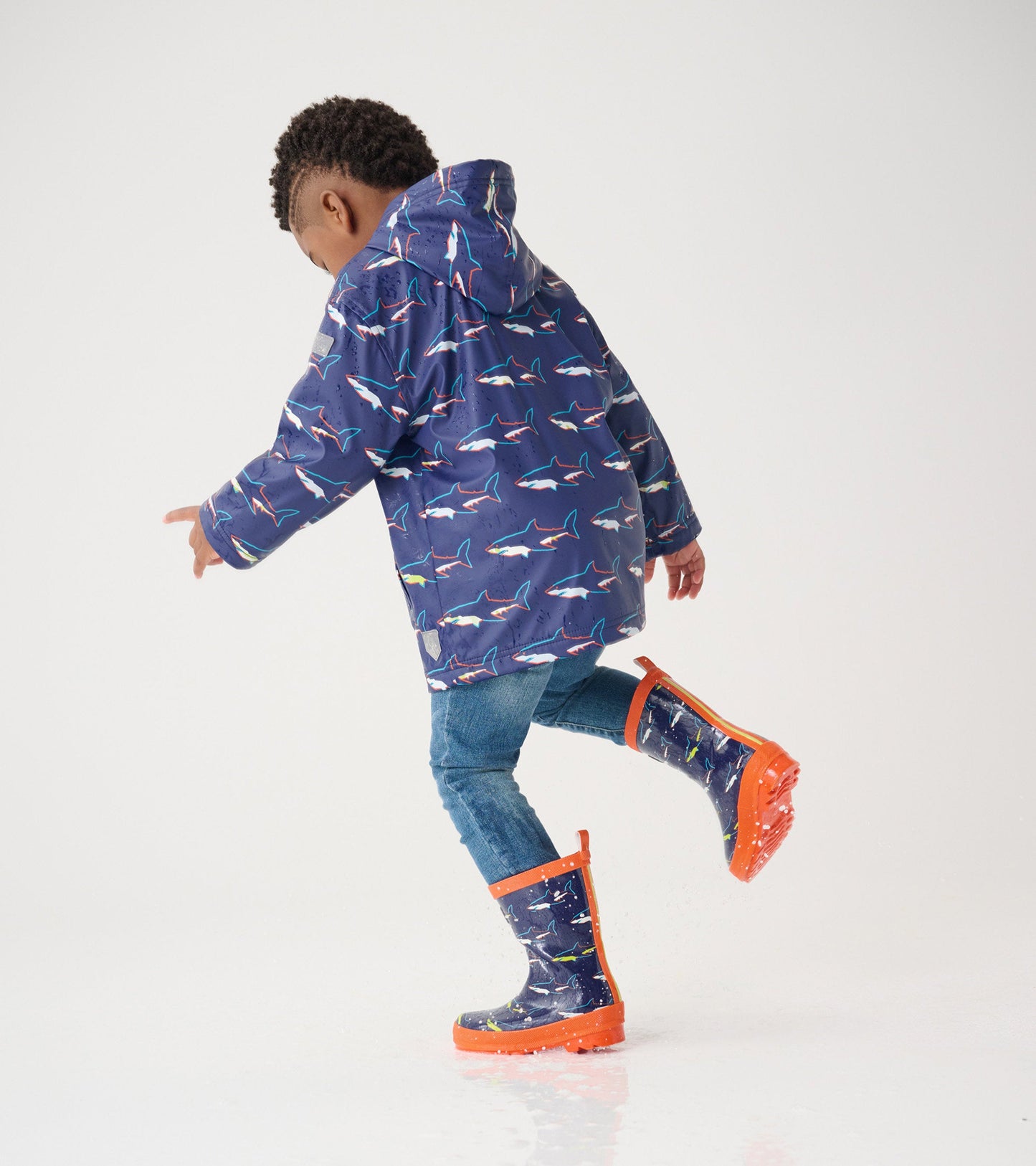Shiny blue wellies with shark pattern and orange trim, worn by a child splashing in water.