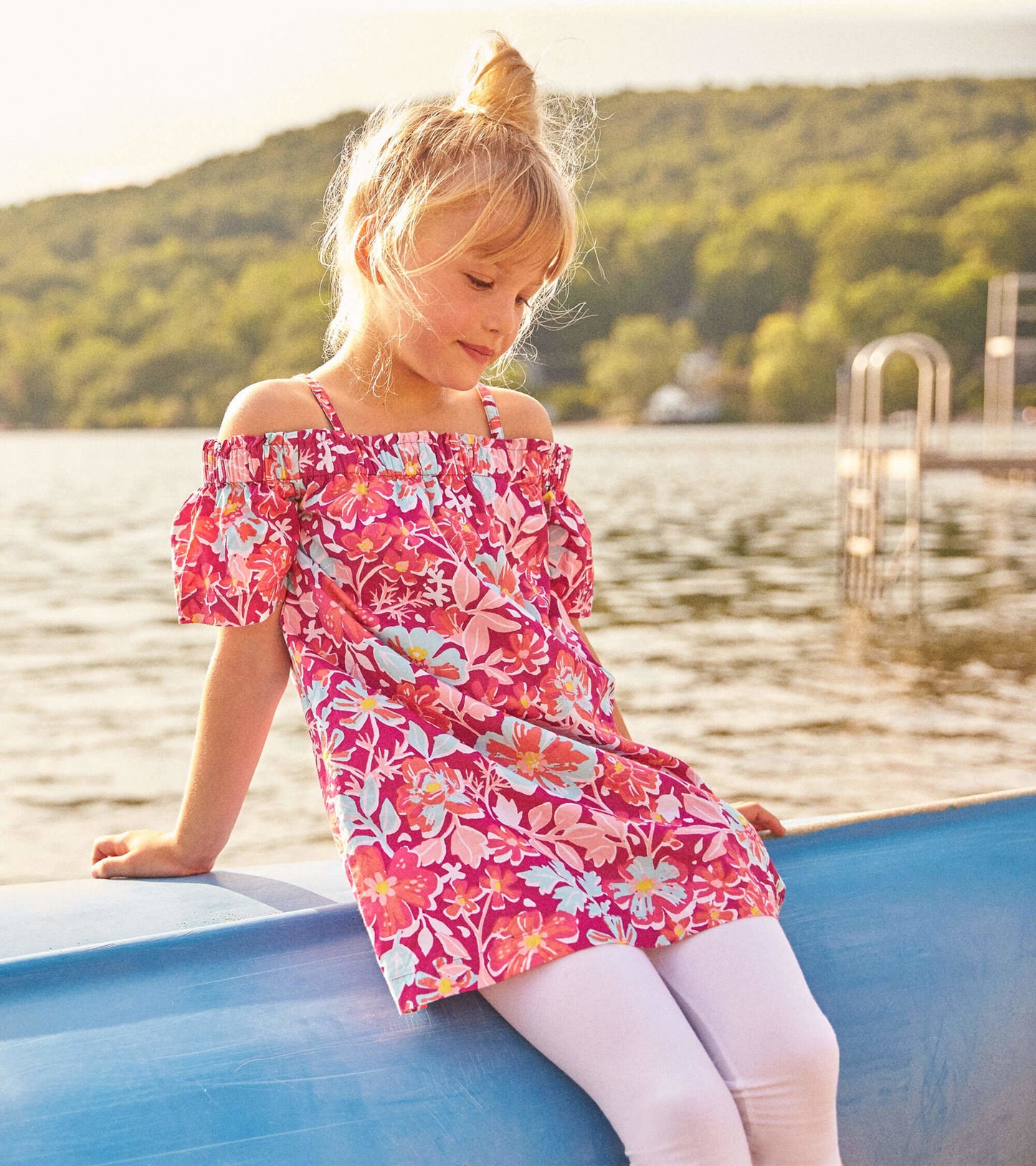 Off-shoulder dress with vibrant pink floral pattern, short puff sleeves, worn by a girl sitting by the water.