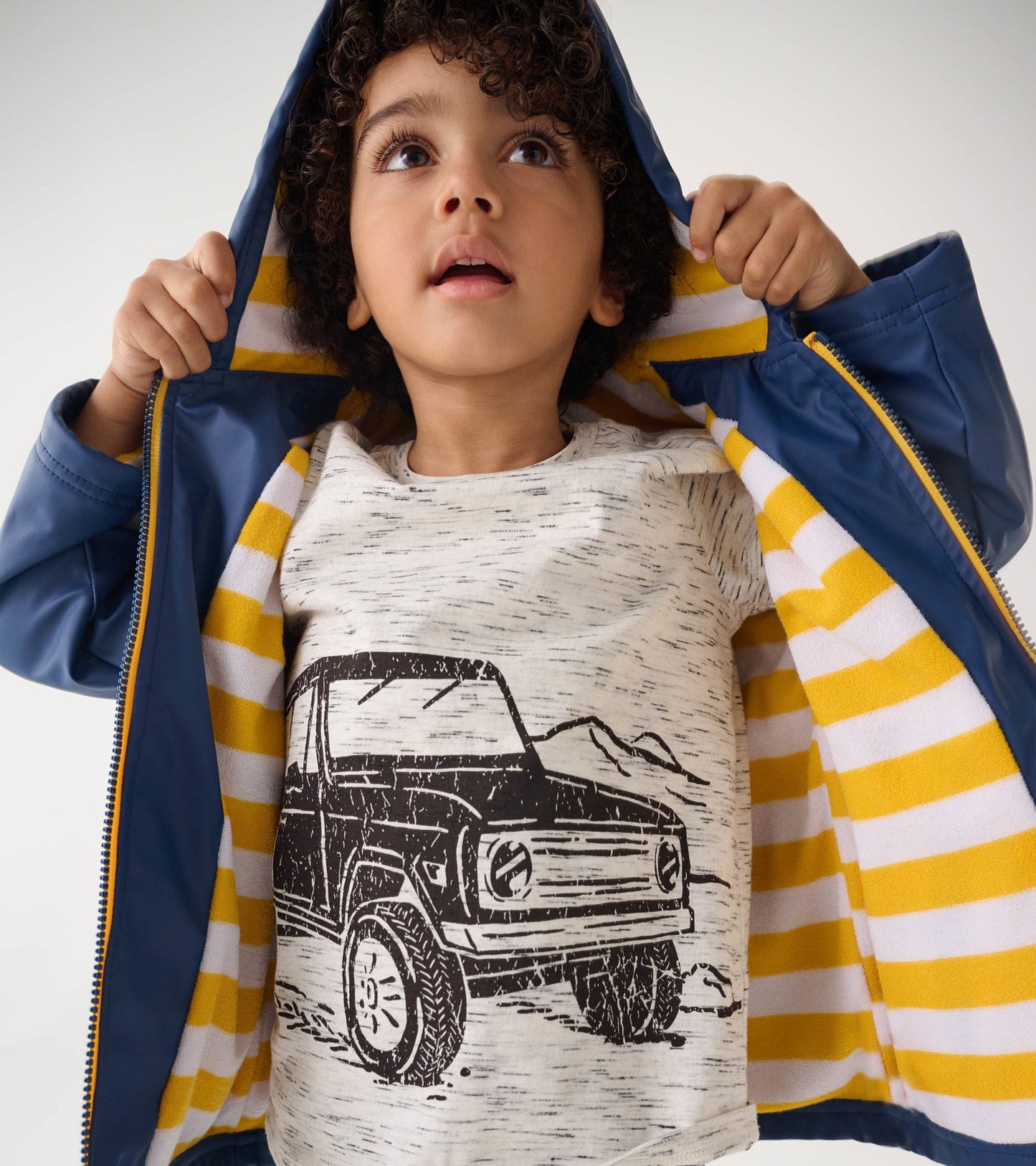 Navy zip-up raincoat with a striped yellow and white lining, worn by a child looking up.