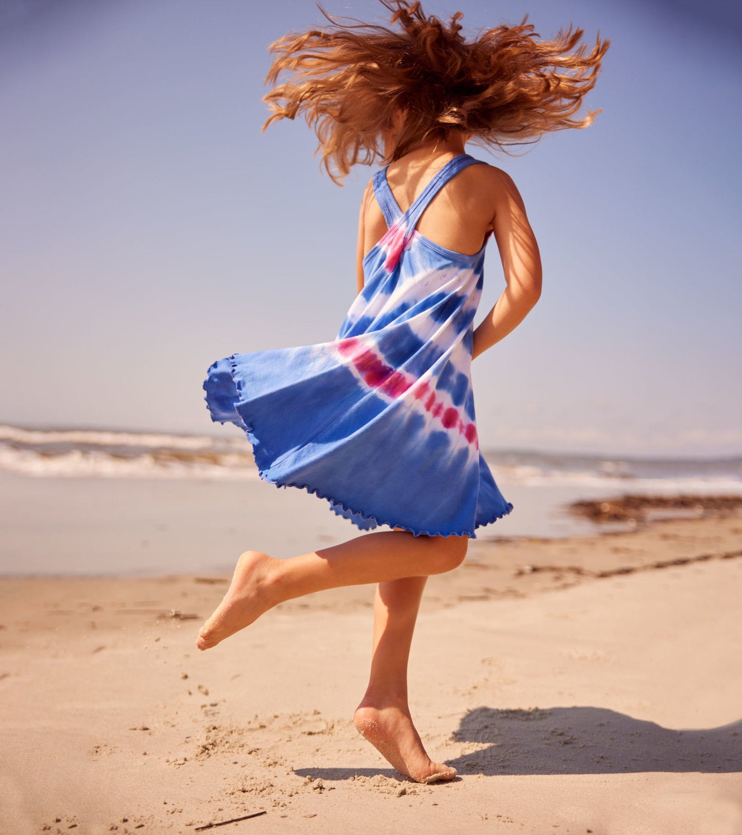 Blue tie-dye trapeze dress with a scalloped hem, worn by a child running on the beach.
