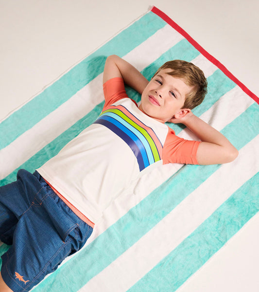 Short sleeve rashguard featuring a white body with colorful horizontal stripes and orange sleeves, laid on a striped towel.