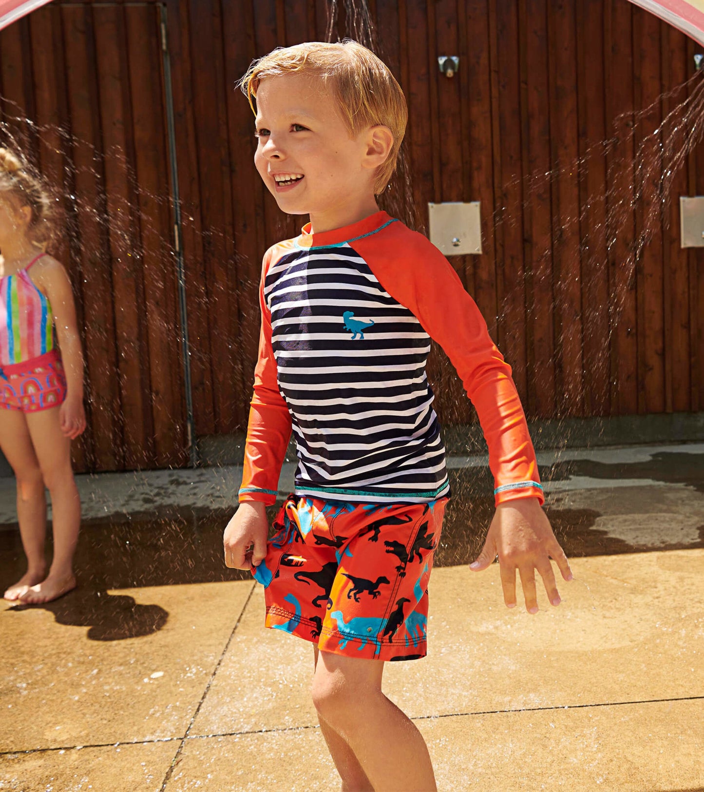 Colorful board shorts featuring dinosaur silhouettes, paired with a striped long-sleeve rash guard, ideal for water play.