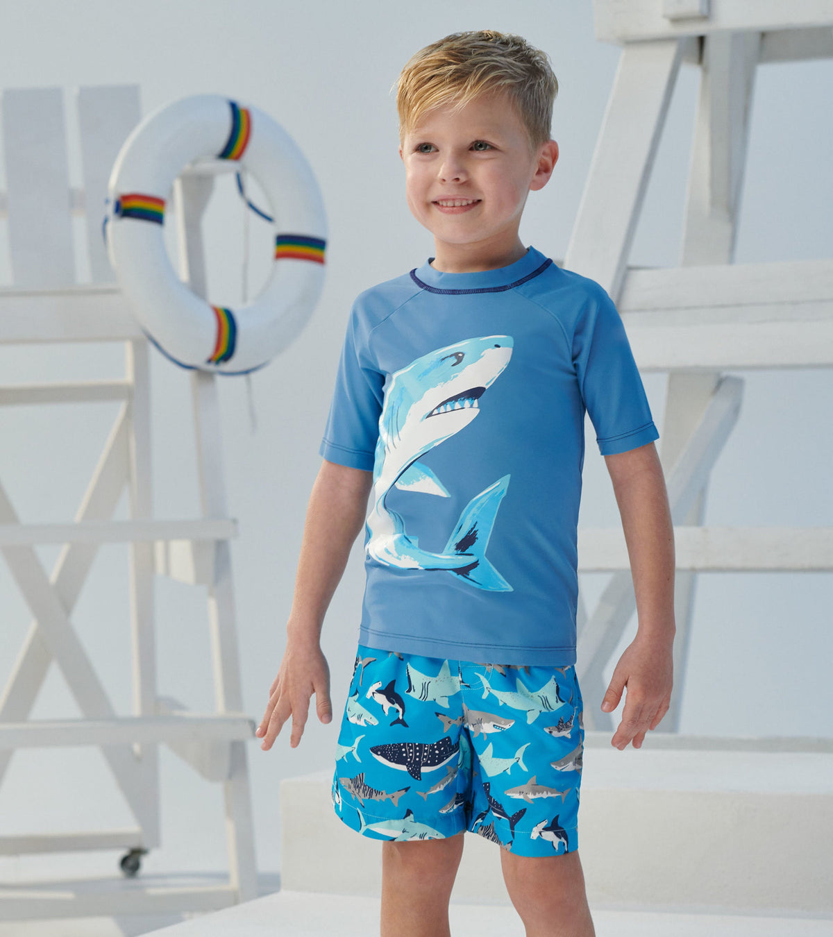 Light blue short sleeve rashguard featuring a shark graphic, paired with blue shark-patterned swim shorts.