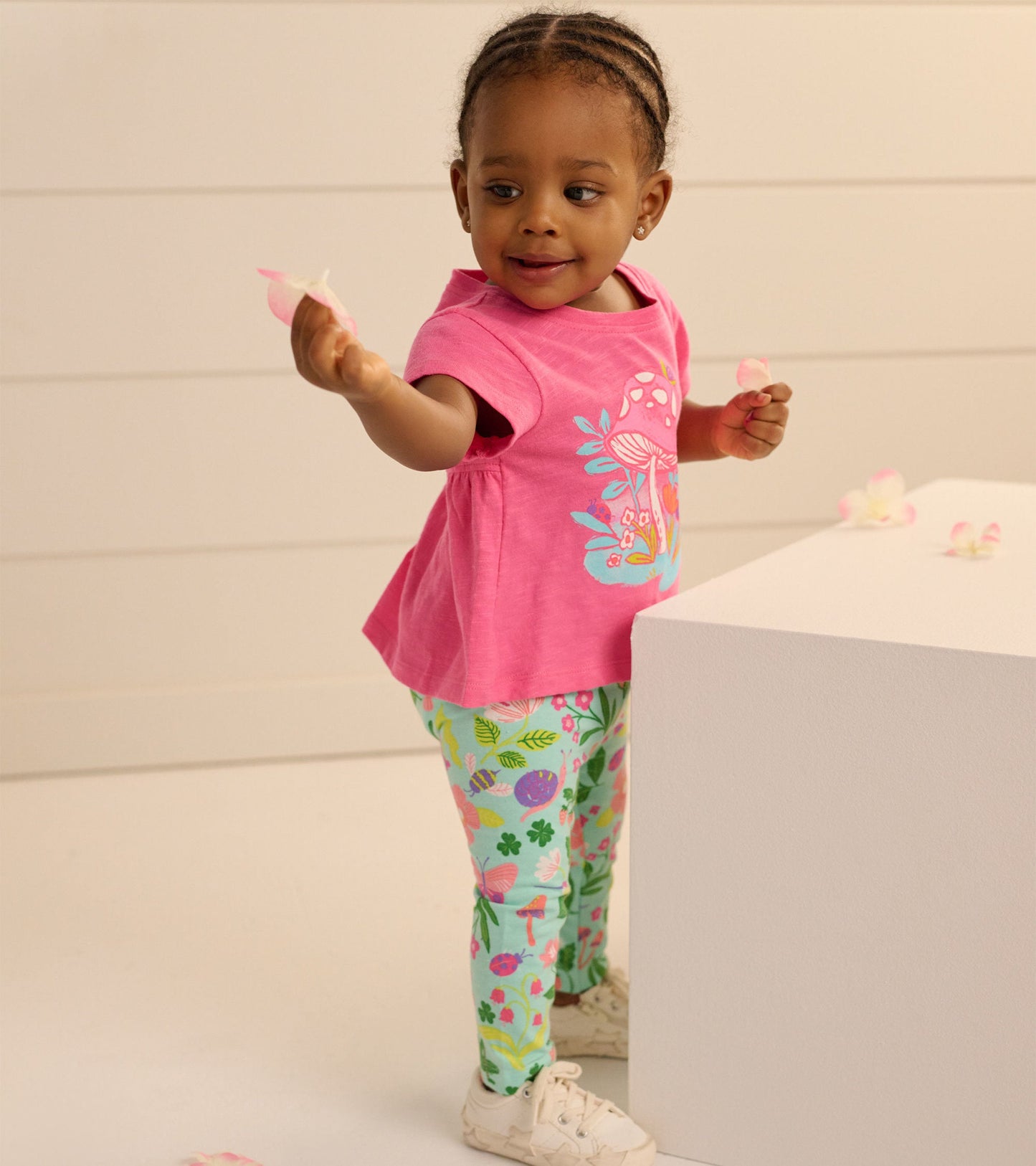 Pink short-sleeve baby tee with floral design paired with green leggings featuring colorful patterns, worn by a toddler.