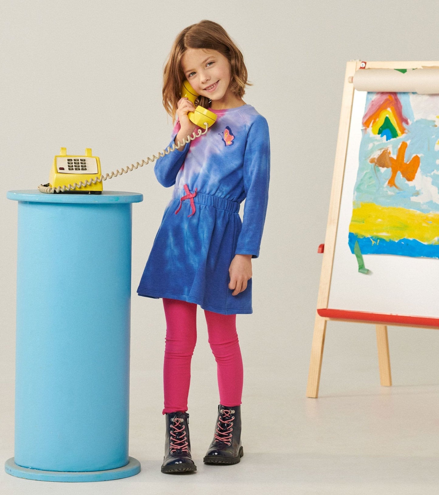 Blue tie-dye cinched waist dress with long sleeves, paired with pink leggings and black boots, worn by a girl.