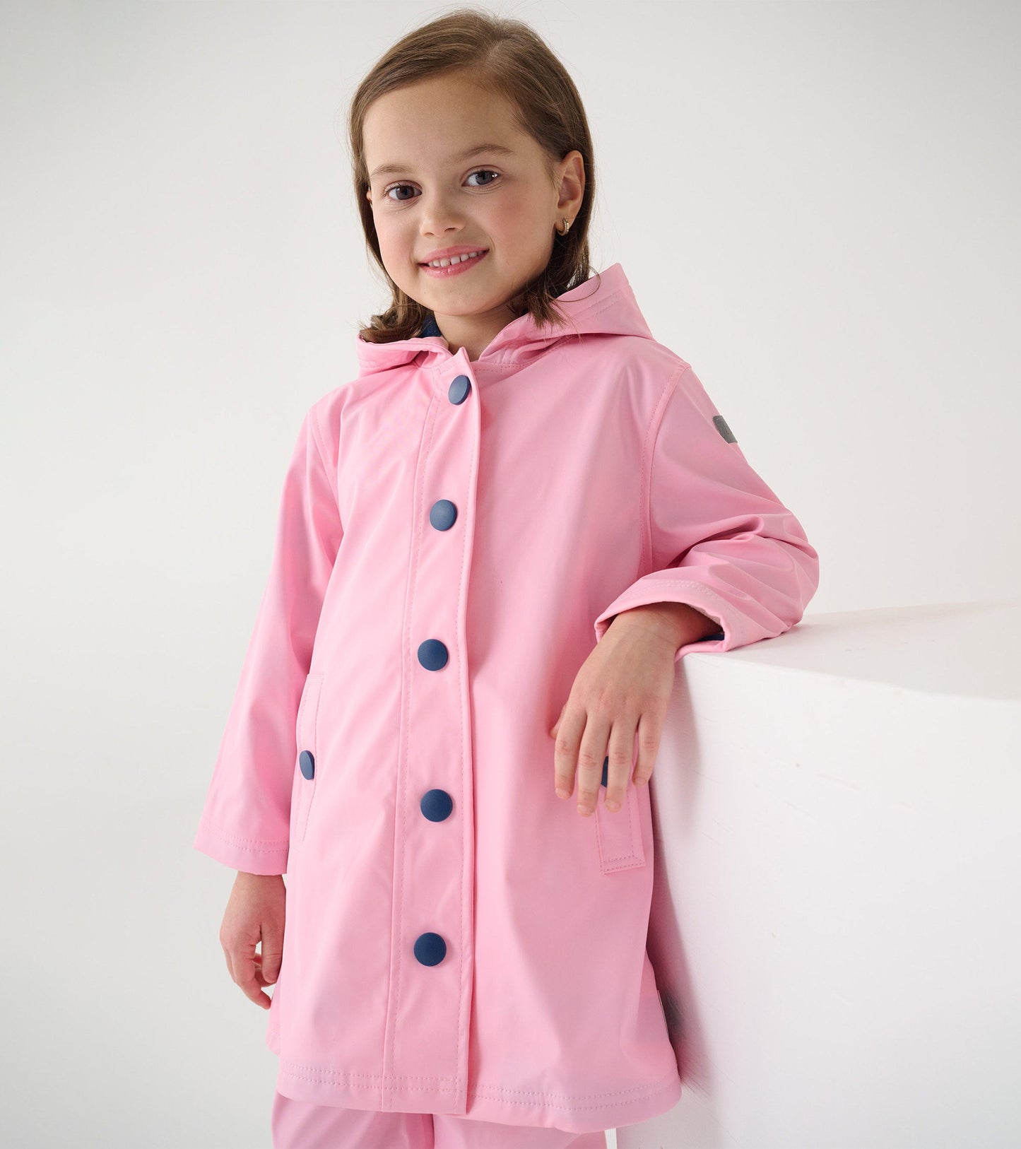 Pink button-up raincoat with navy buttons and a hood, designed for girls, featuring a relaxed fit and side pockets.