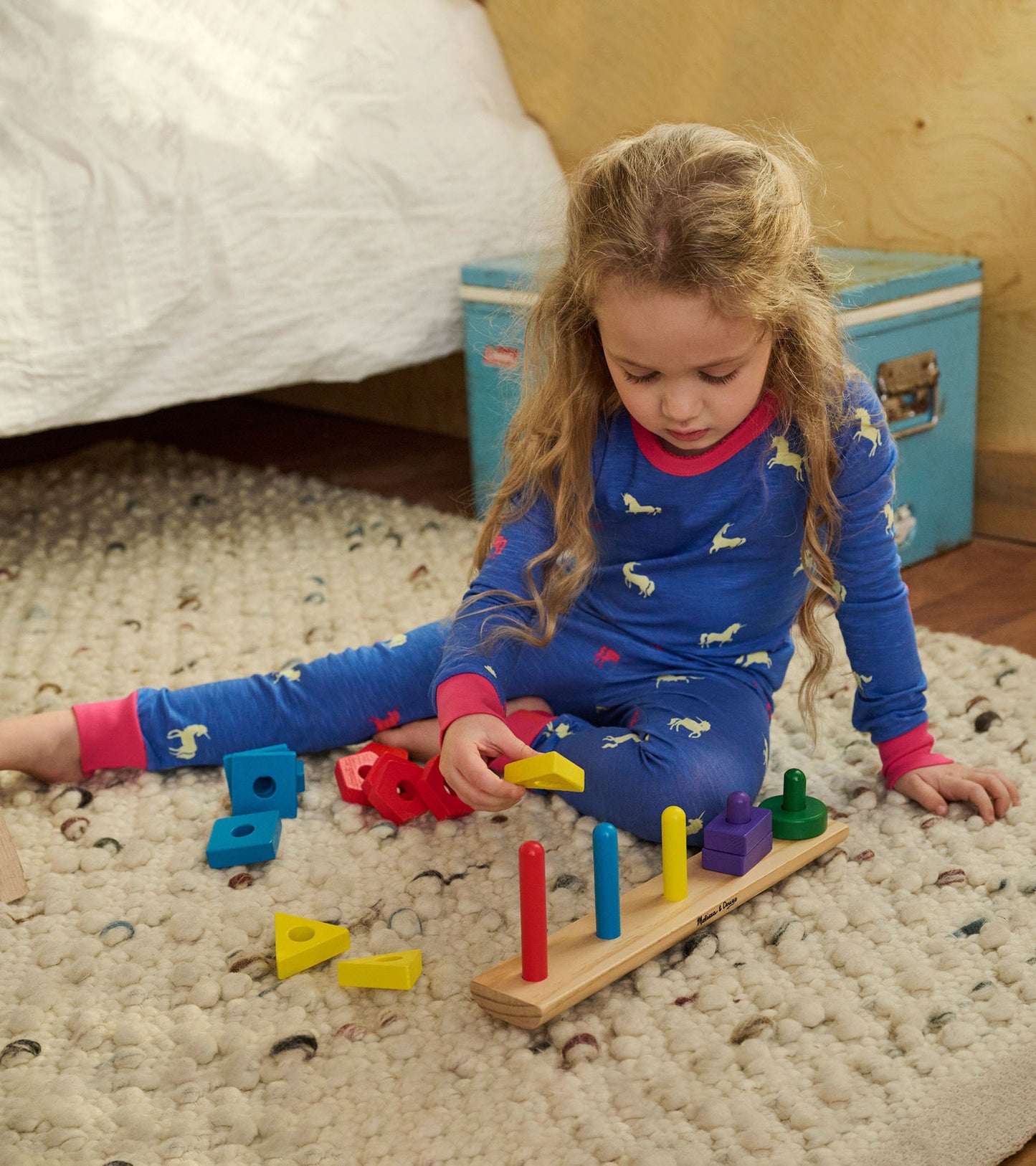 Blue pajama set with unicorn print, featuring pink cuffs, worn by a girl playing with colorful geometric blocks on a rug.