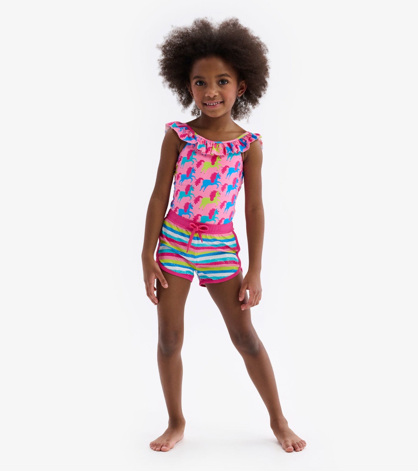 Colorful swim shorts featuring rainbow stripes and a drawstring waist, paired with a pink unicorn-patterned top.