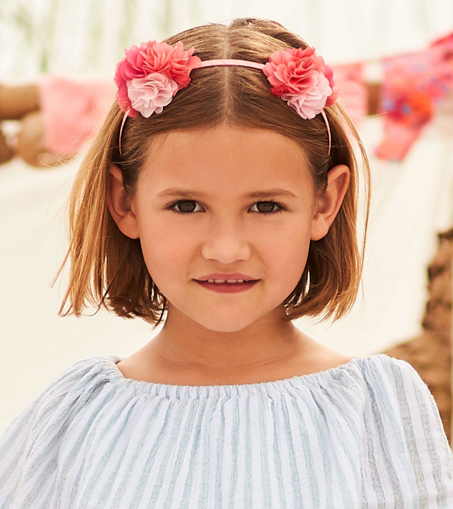 Floral headband featuring pink and coral flowers on a thin elastic band, suitable for kids.